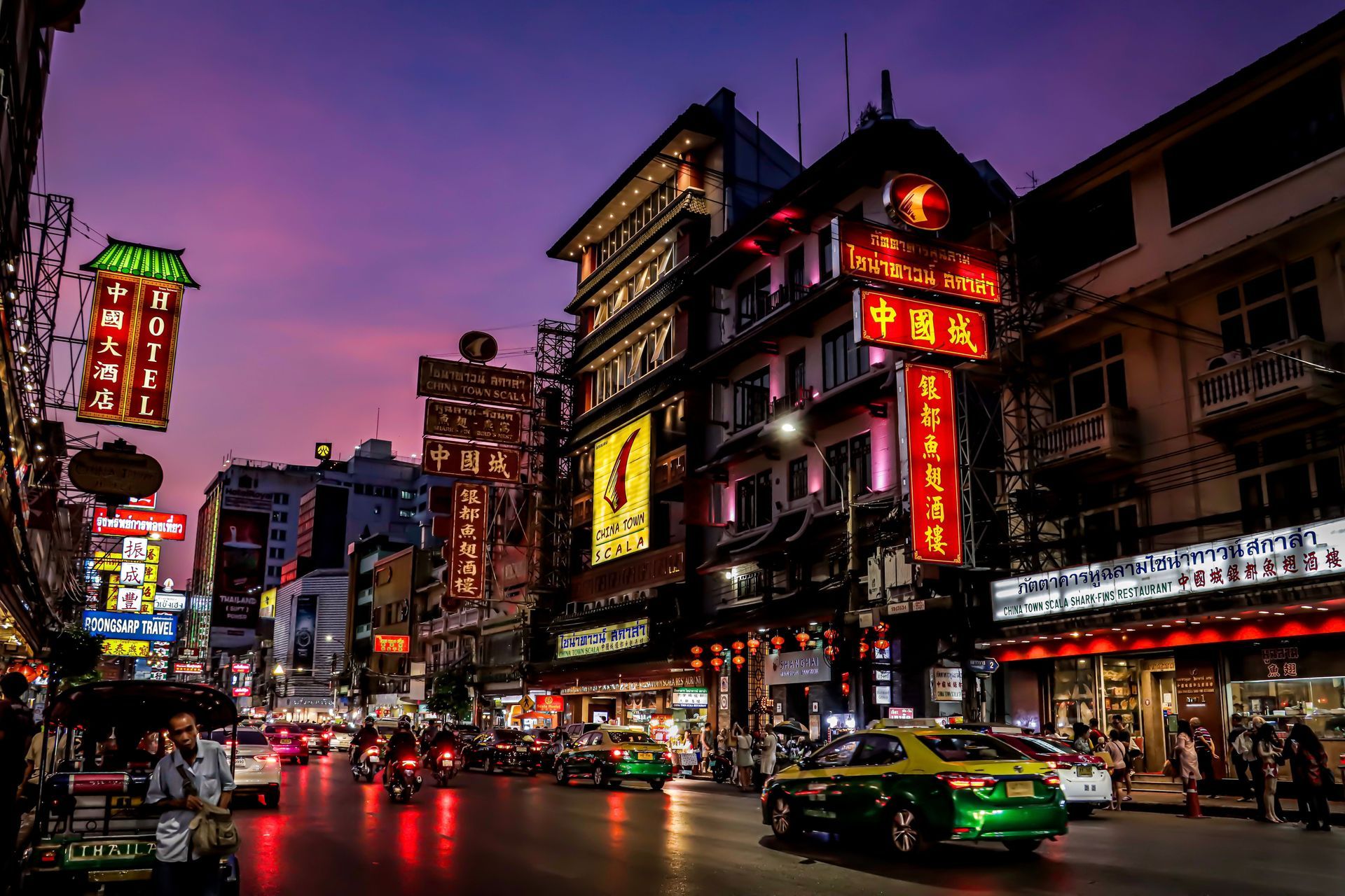 Busy neon-lit city street at dusk with cars, storefronts, and glowing signs in an East Asian district