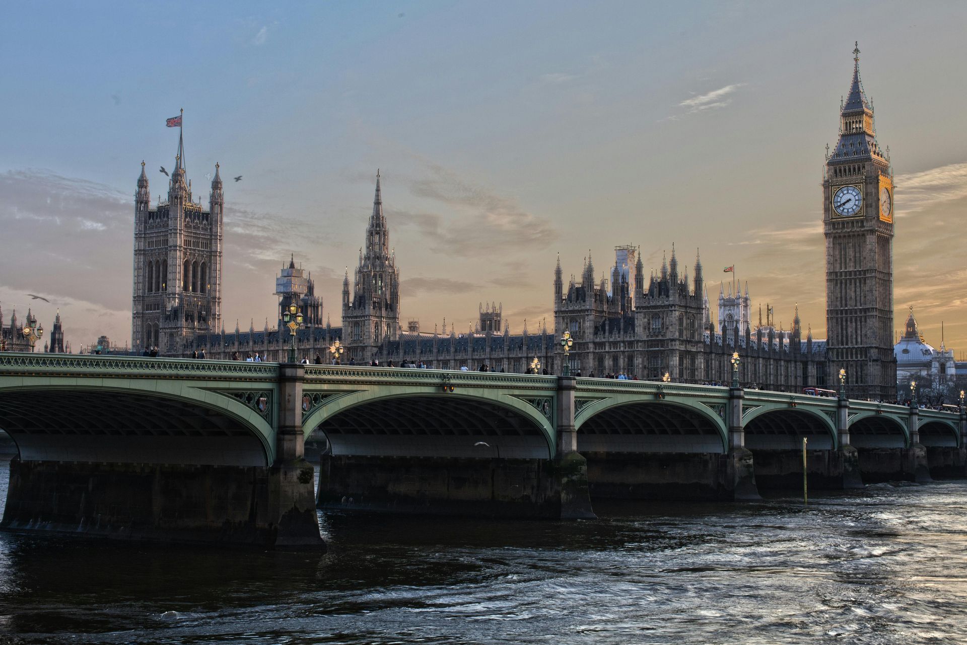 Westminster Bridge and the Houses of Parliament at dusk beside the Thames, with Big Ben lit up.