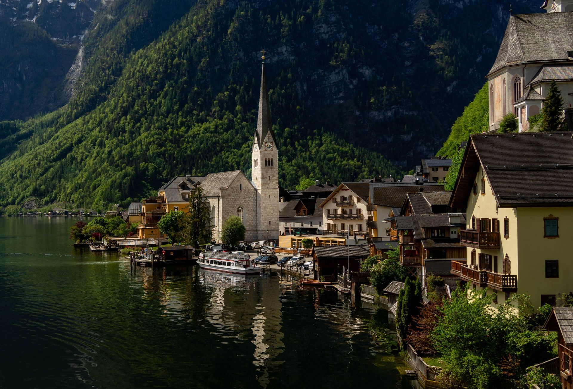 Lakeside village with church steeple beside calm water, backed by steep green mountains