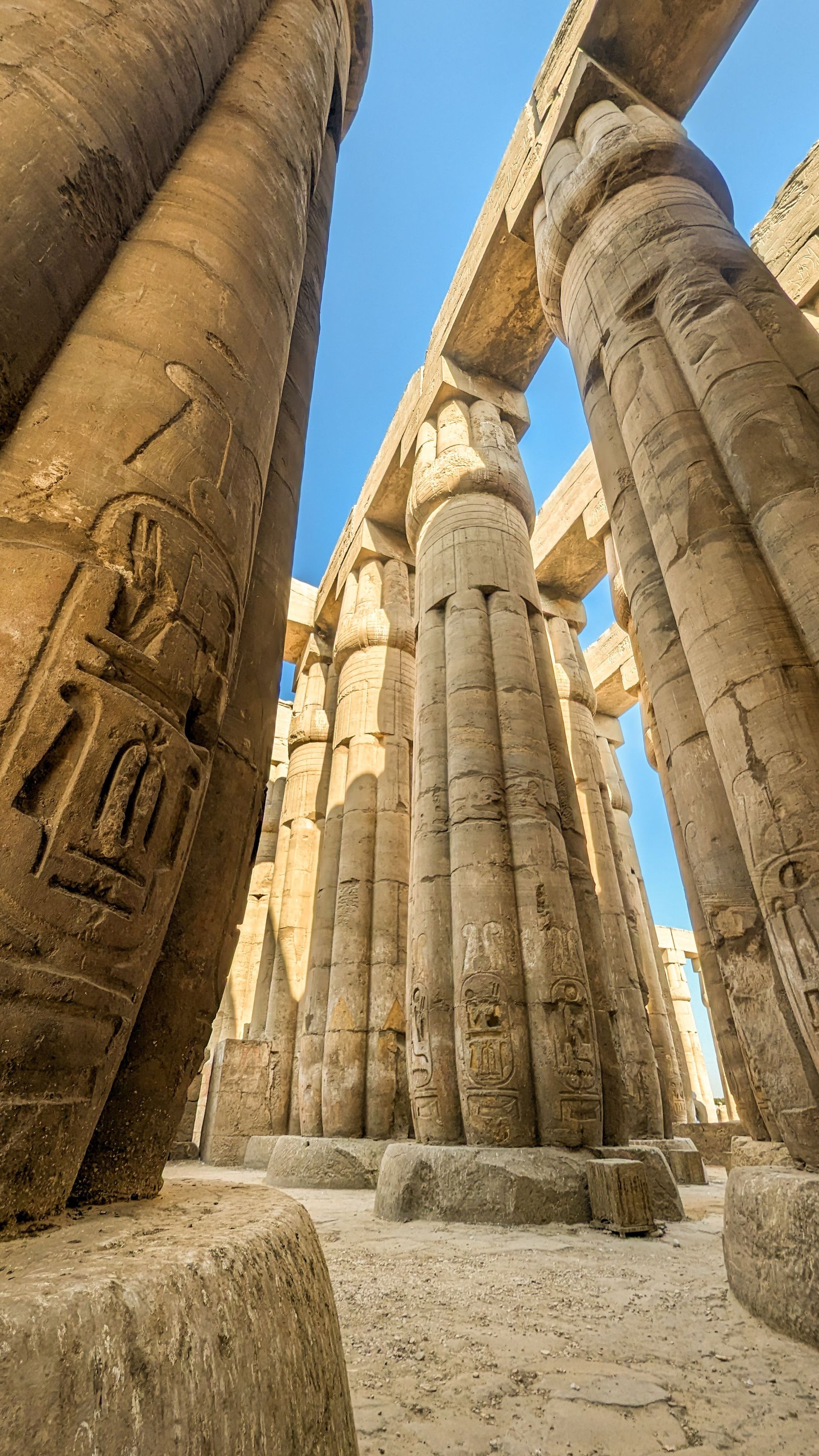 Ancient stone temple columns with carved hieroglyphs under a bright blue sky