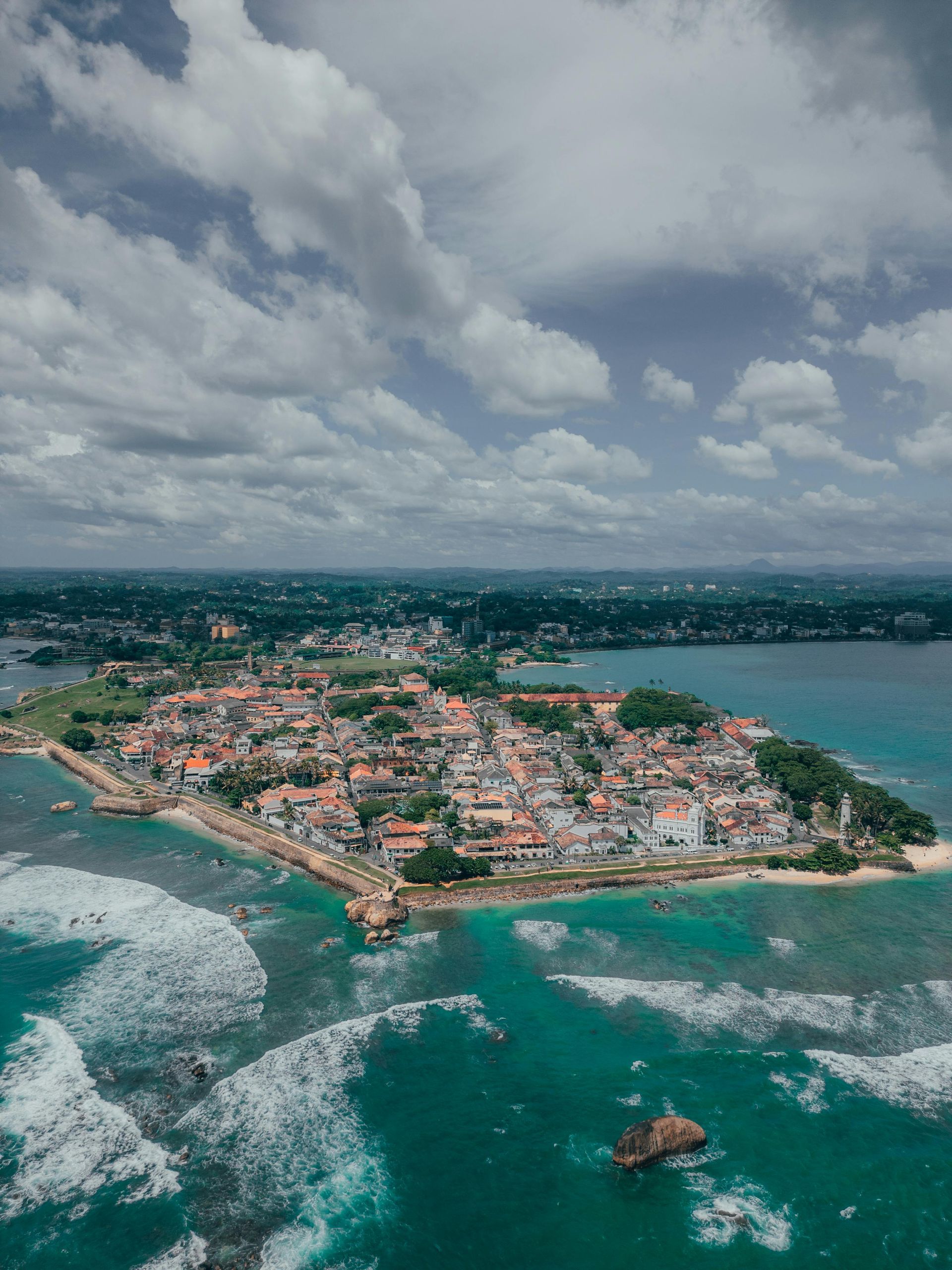 Aerial view of Galle Fort in Sri Lanka, a coastal city with buildings and surrounding ocean waters under a cloudy sky.