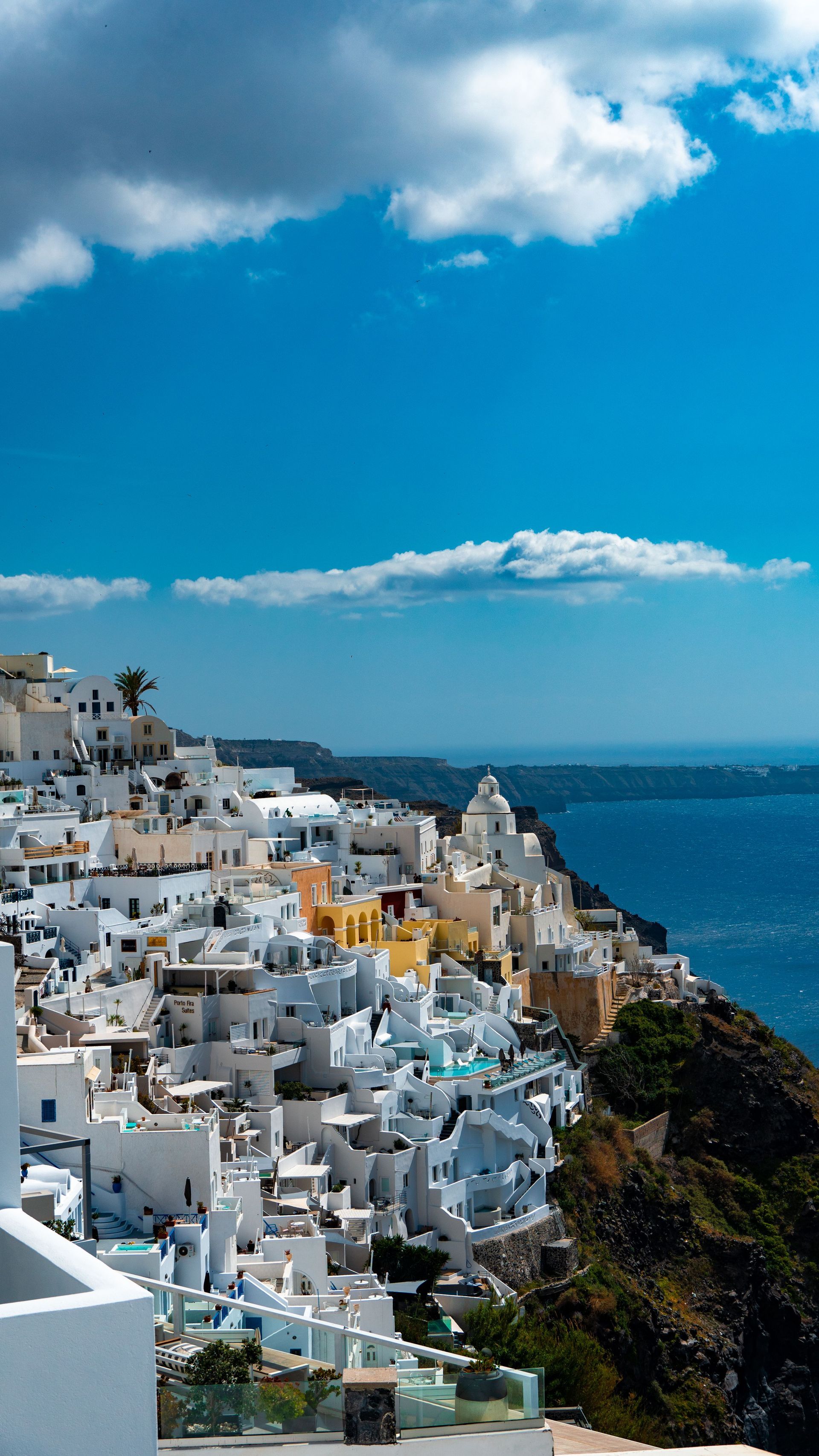 White hillside buildings overlooking a blue sea under a bright sky with clouds
