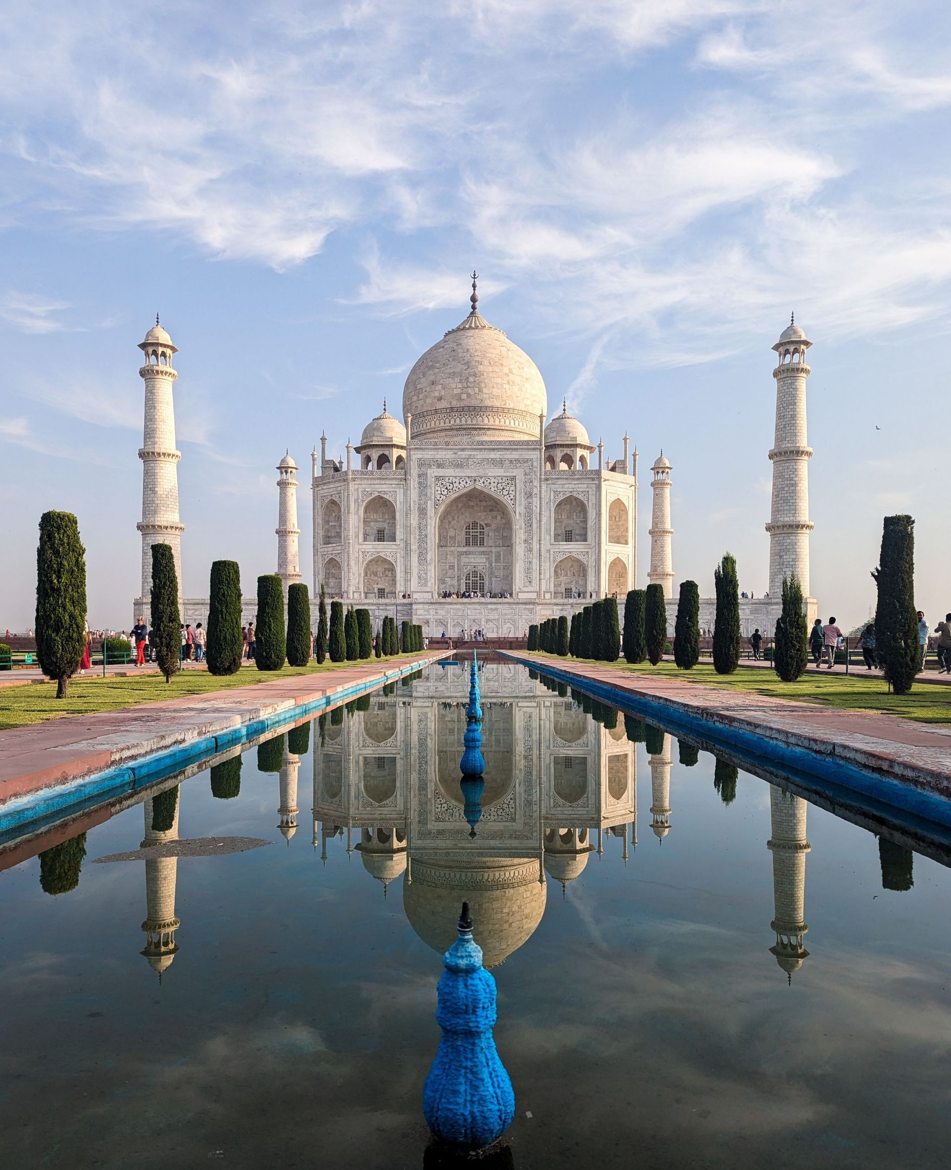 Taj Mahal reflected in a long pool, with a peacock in the foreground and blue sky above.