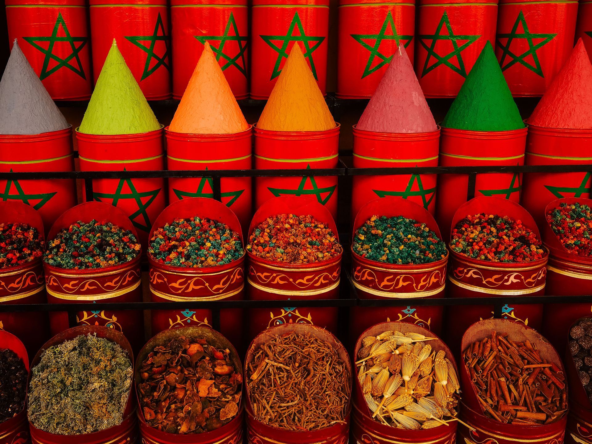 Colorful spice cones displayed in rows in a market stall with red background and woven baskets