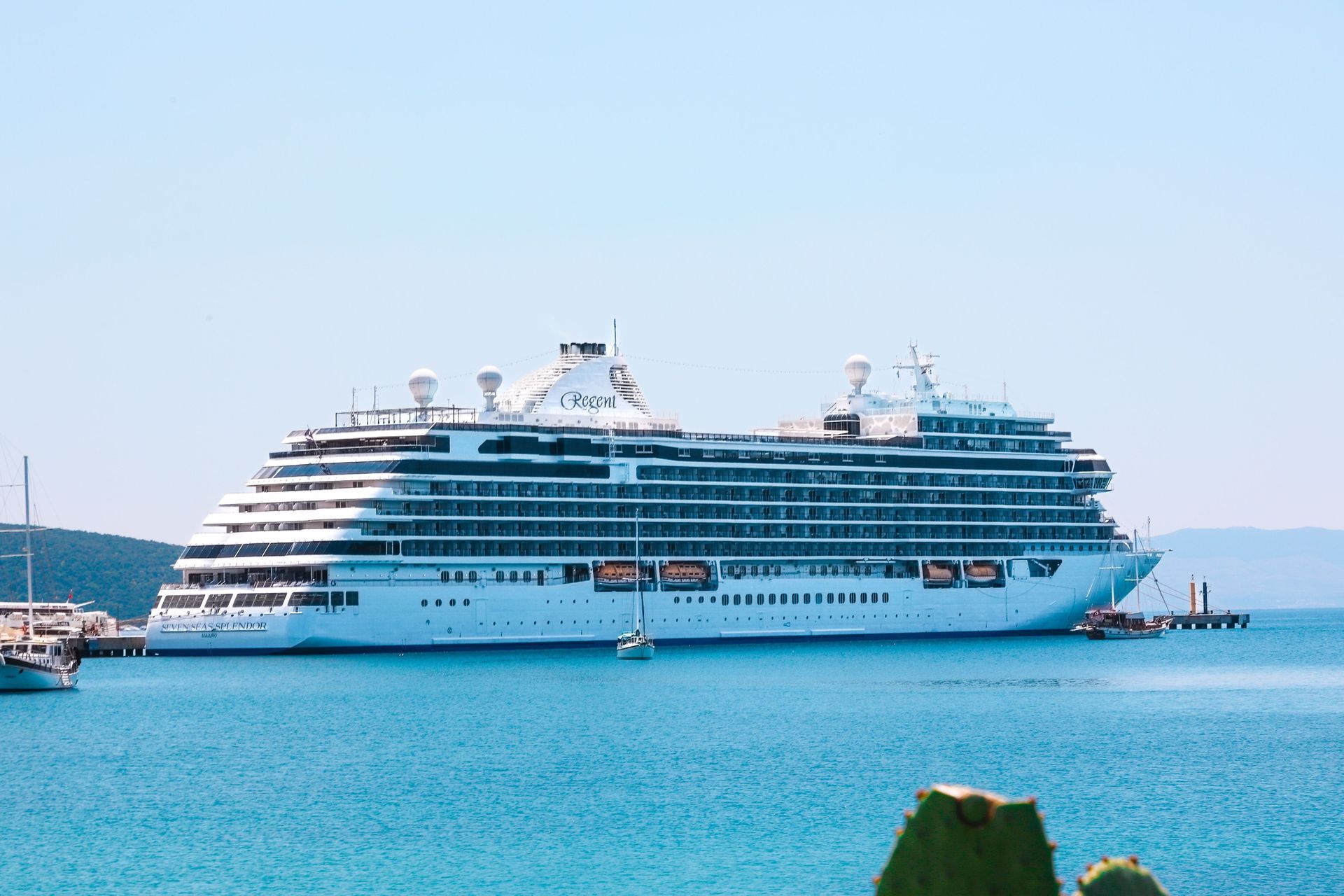 Large white cruise ship docked in turquoise water under a clear blue sky