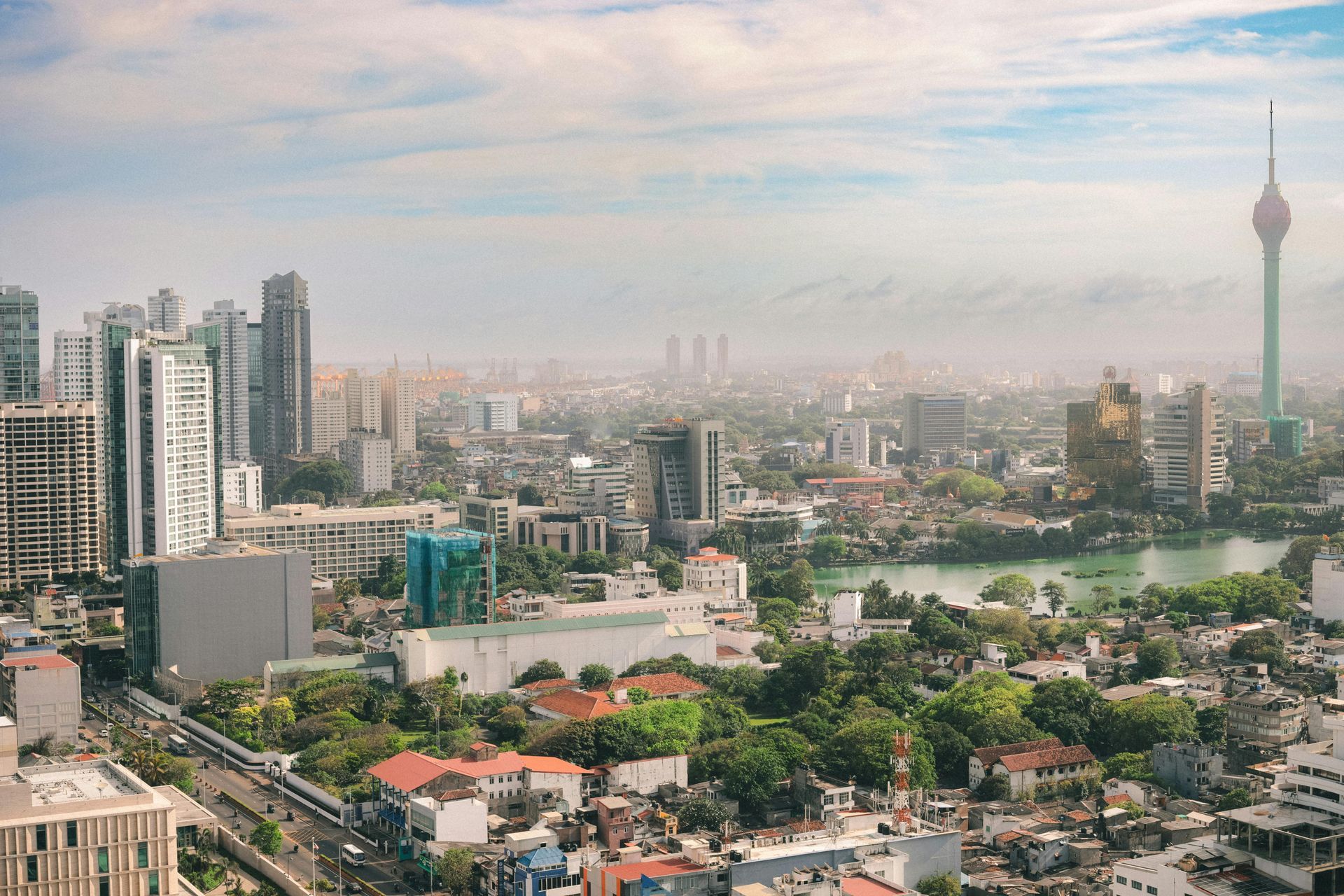 City skyline with high-rise buildings, dense greenery, and a tall tower under a hazy sky.