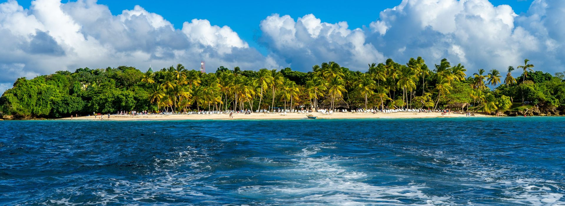 Tropical island with palm trees and a cloudy blue sky above choppy ocean water