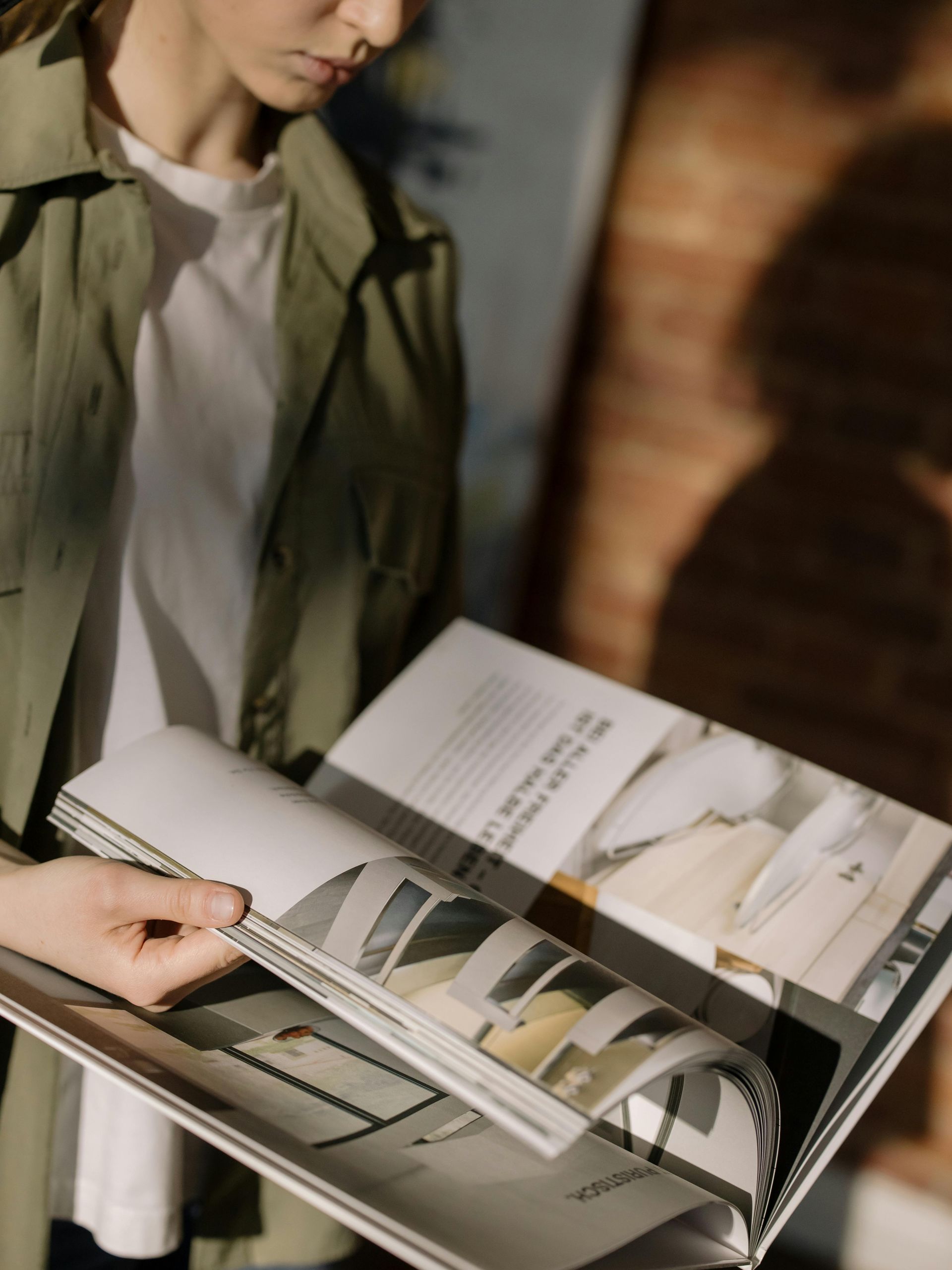 Person browsing a fashion magazine with clothing photos and a notebook on a table