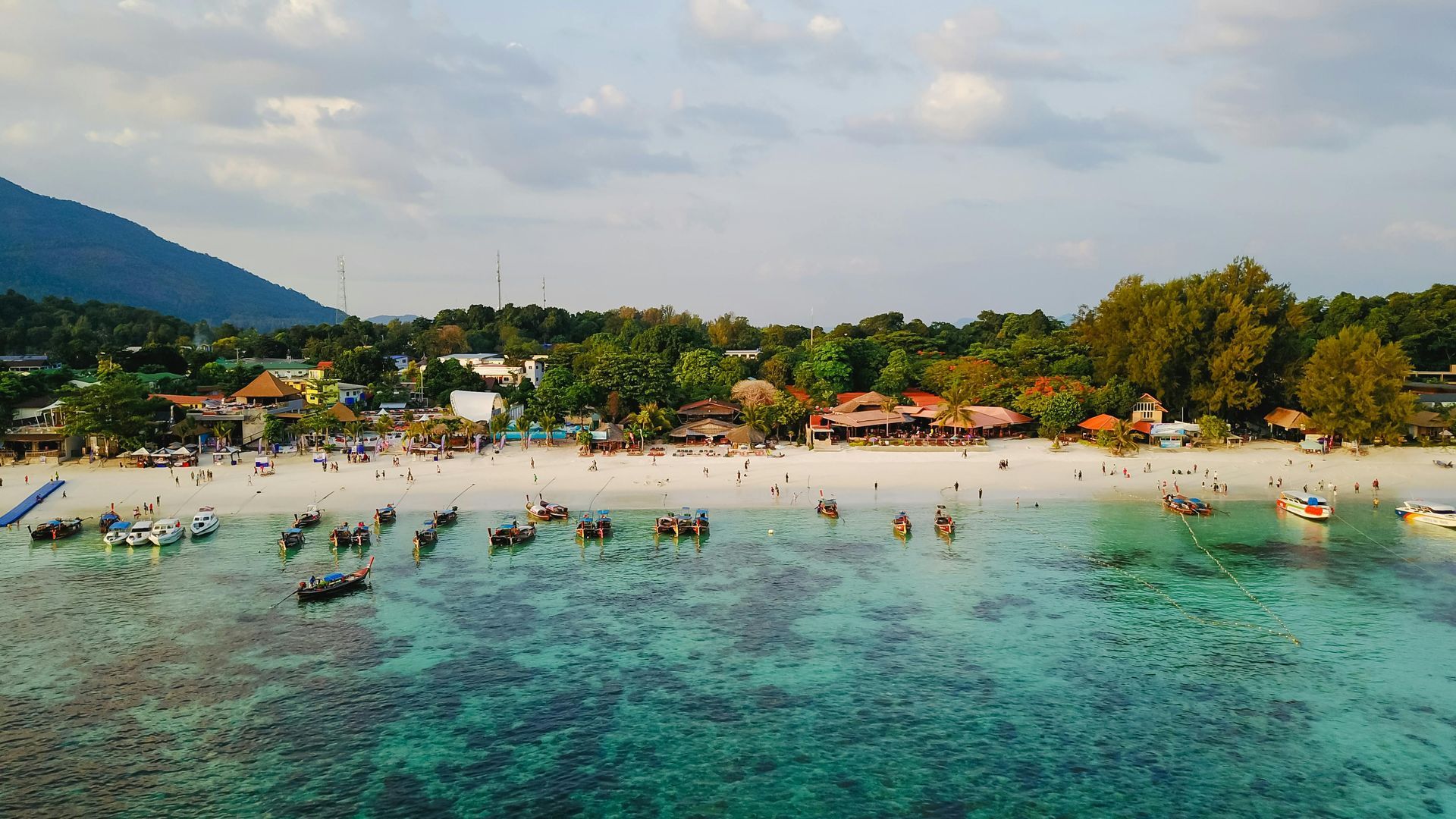 Crowded tropical beach with swimmers, turquoise water, and palm trees along the shore