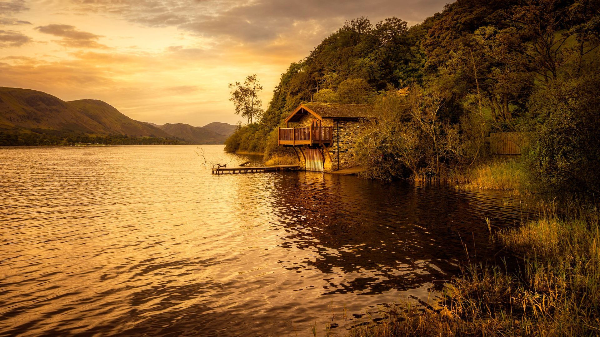 Golden sunset over a calm lake with a small cabin on the shore and forested hills in the background