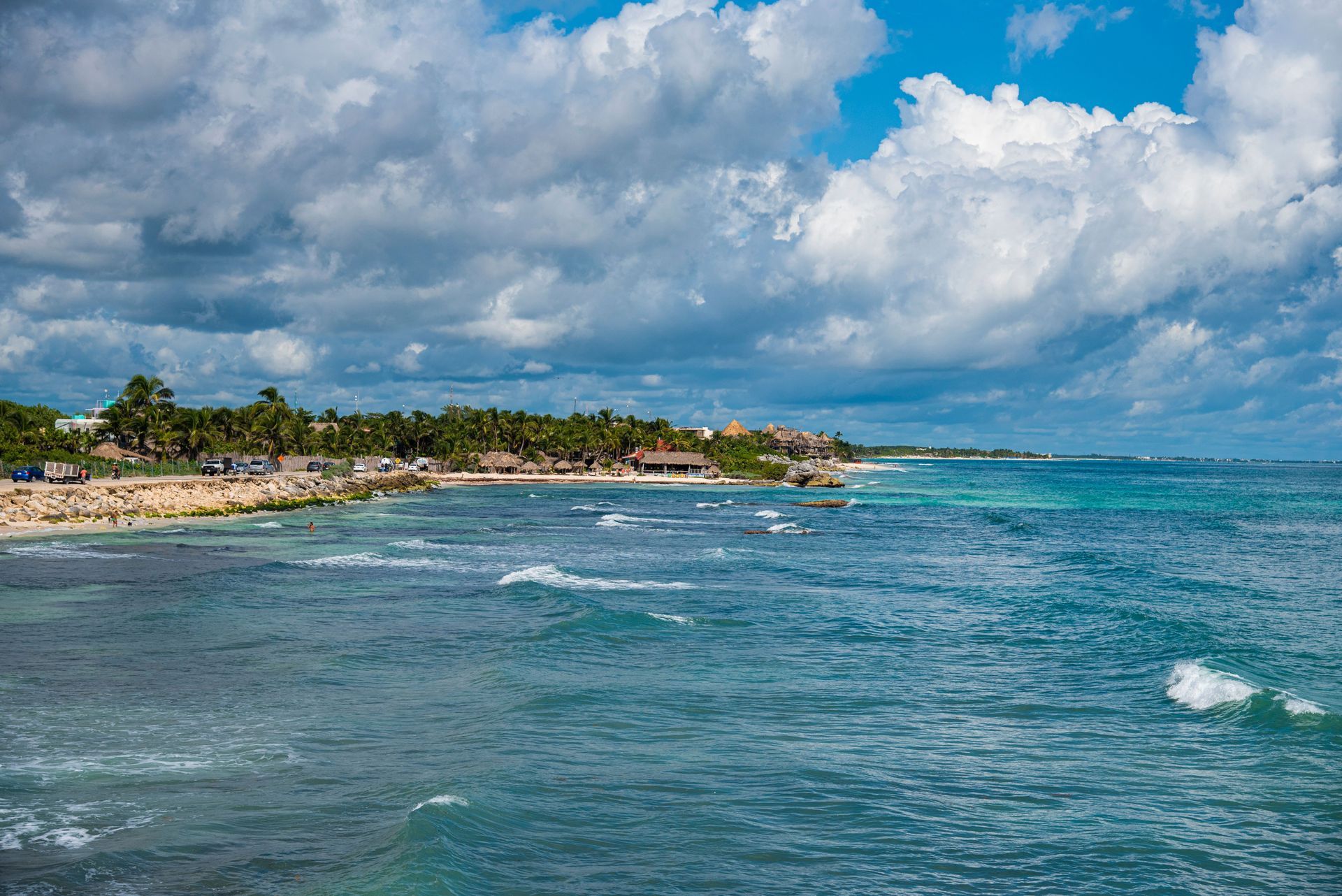 Tropical coastline with turquoise water, sandy shore, and white clouds under a blue sky