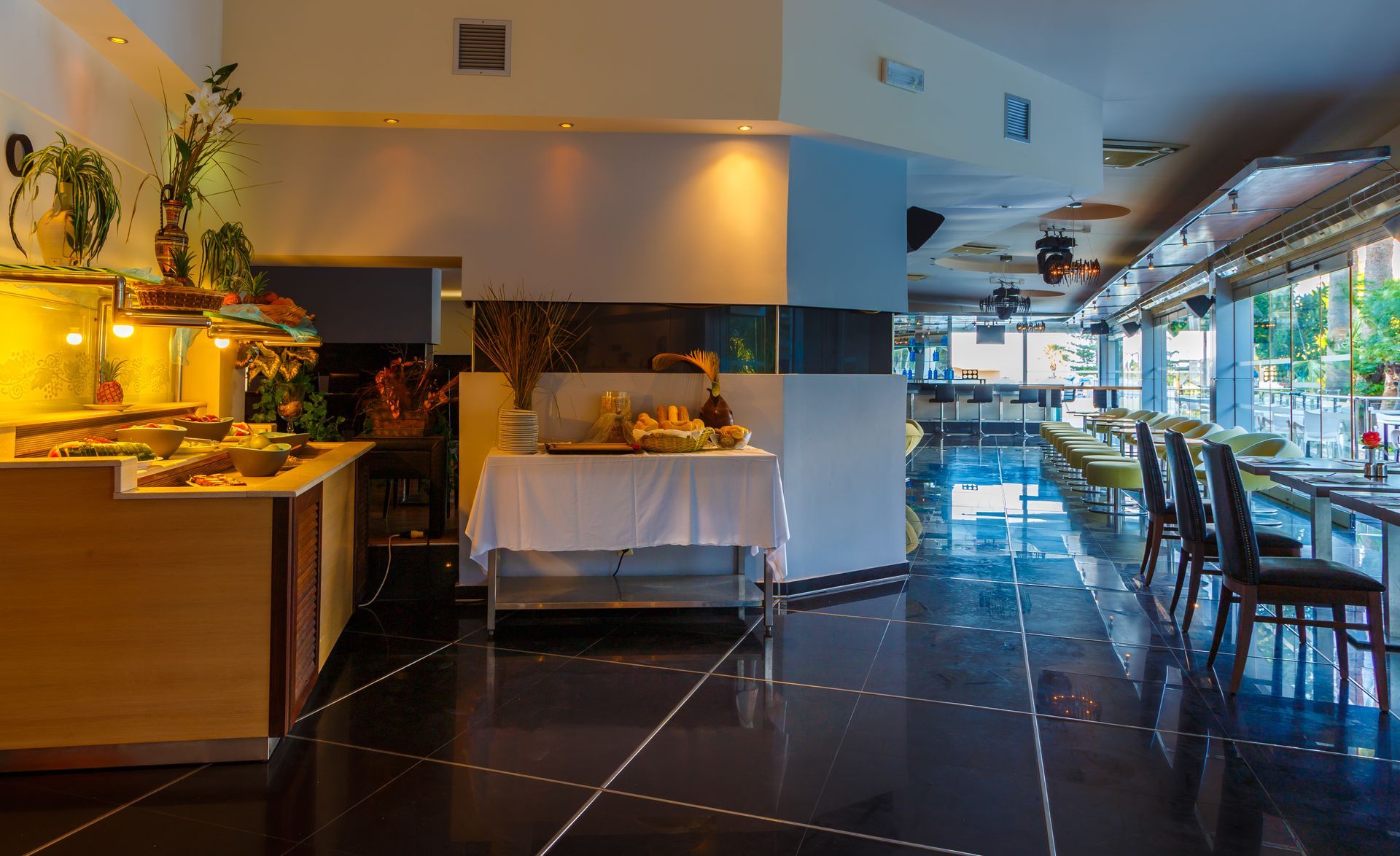 Interior of a modern restaurant with a buffet, tables, and a glossy black floor.