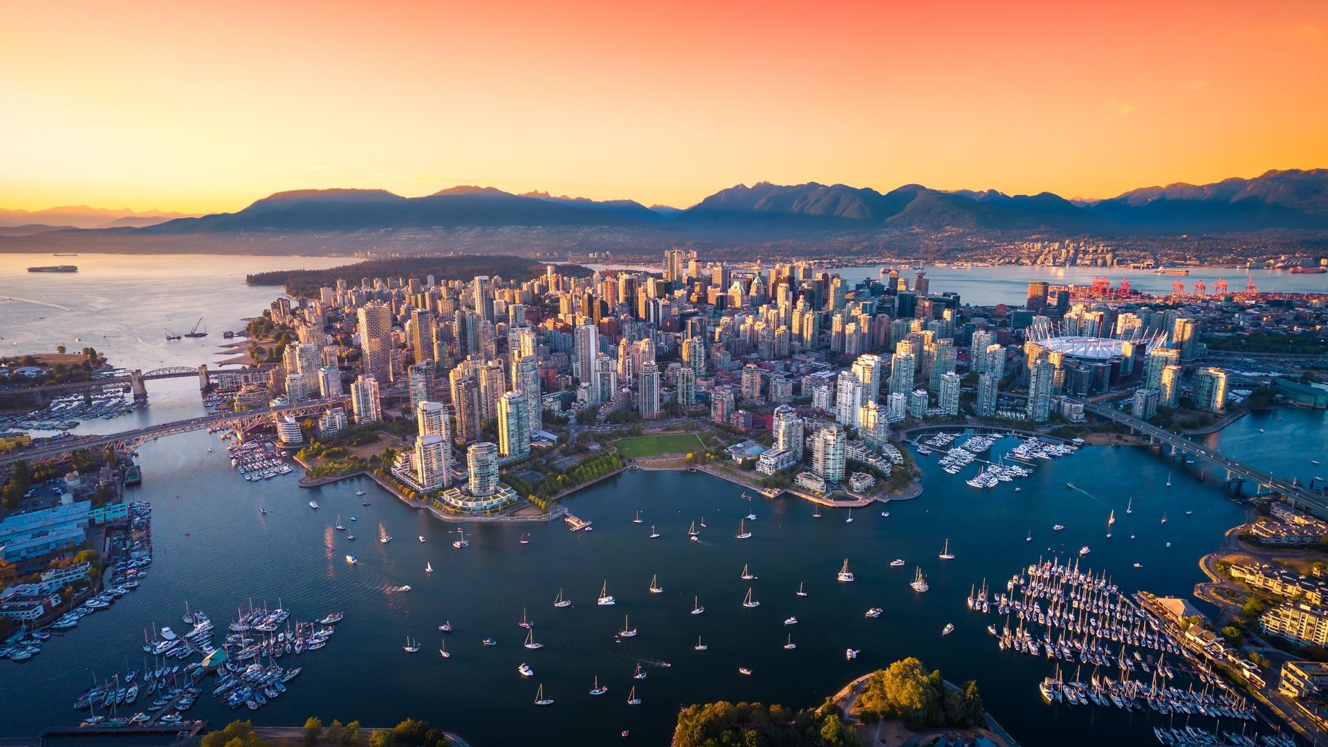 Aerial view of Vancouver, Canada at sunset, skyscrapers and harbor, orange and blue hues.