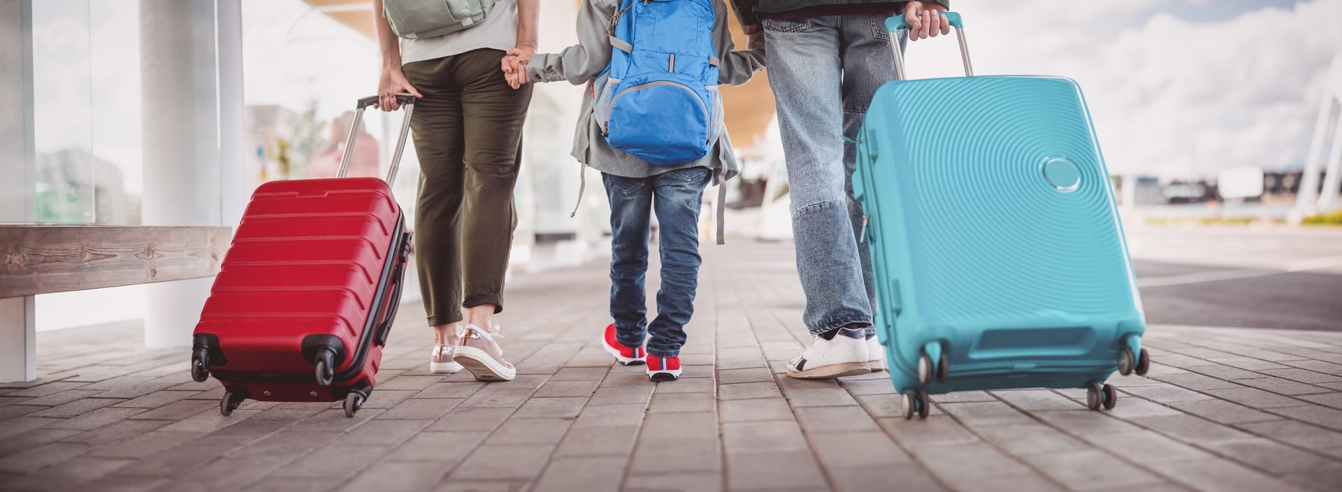 A family walking with suitcases outside, with a red and blue suitcase visible.