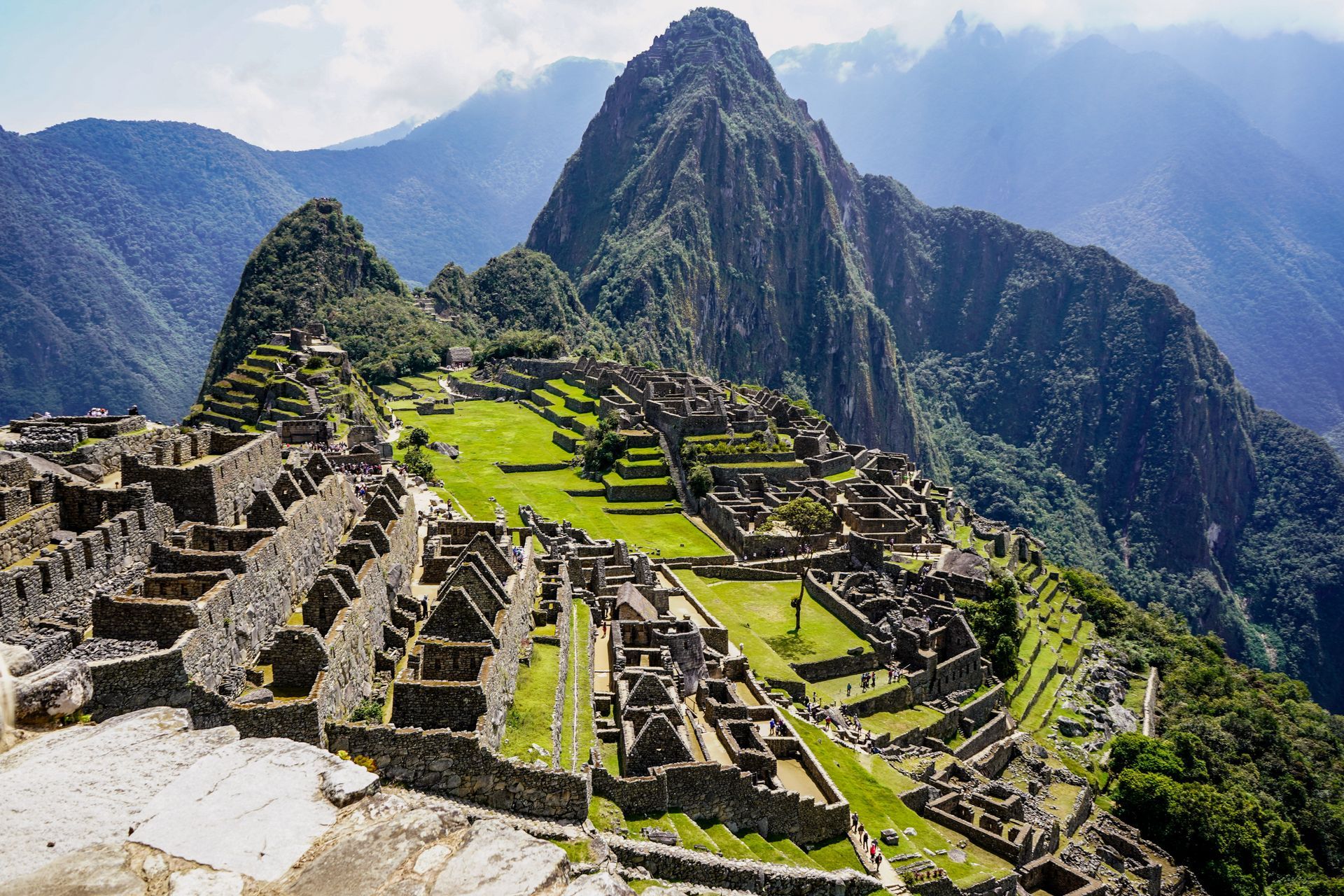 Machu Picchu ruins in Peru, built into a mountainside, with green grass and surrounding peaks.