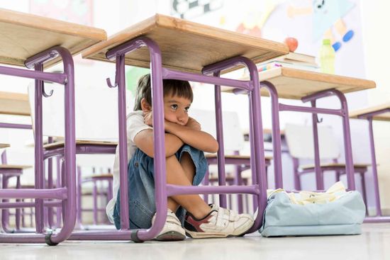A Young Boy Is Sitting Under A Desk In A Classroom – Independence, MO - Mary Hargrave