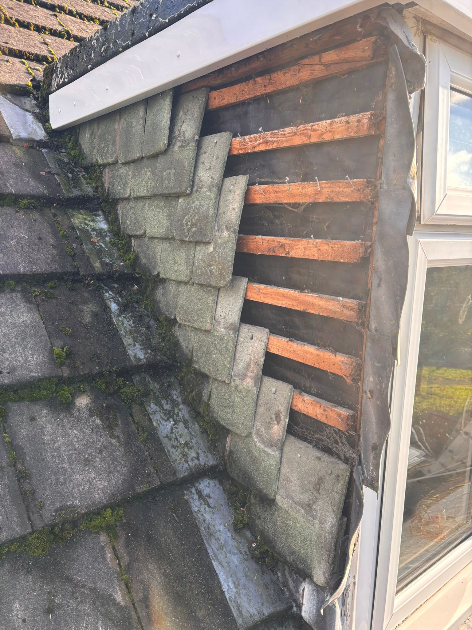 A section of a roof with missing tiles, revealing the underlying wooden battens and black waterproof membrane.