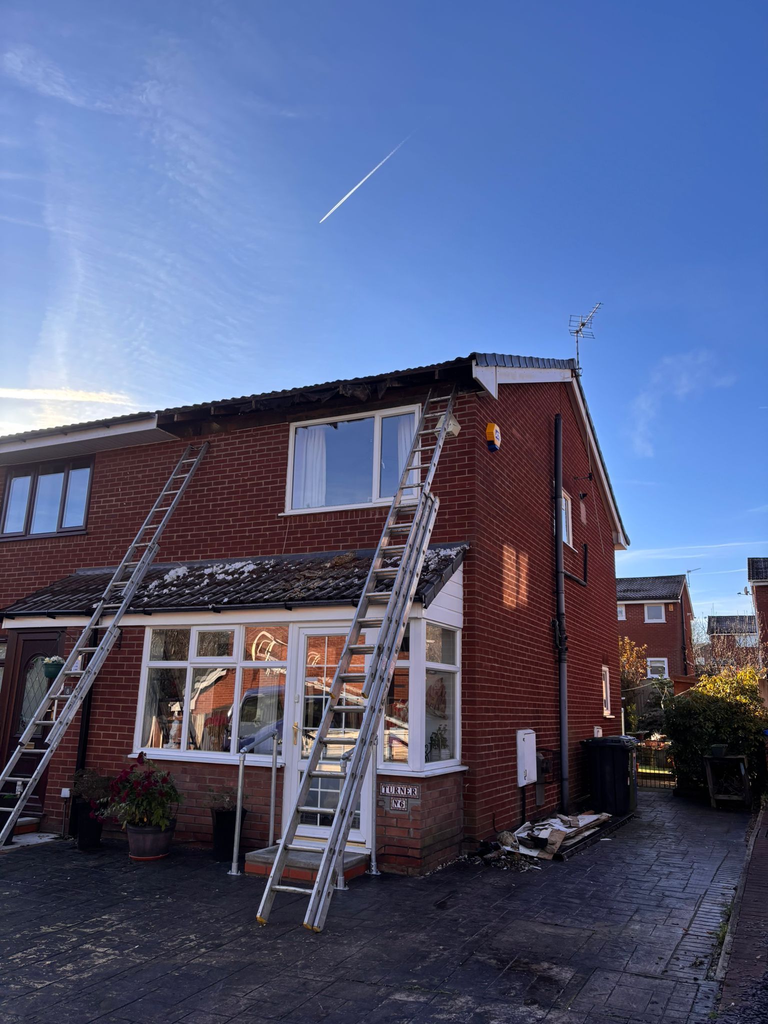 Two extension ladders are propped against the front of a two-story red brick house on a clear, sunny day.
