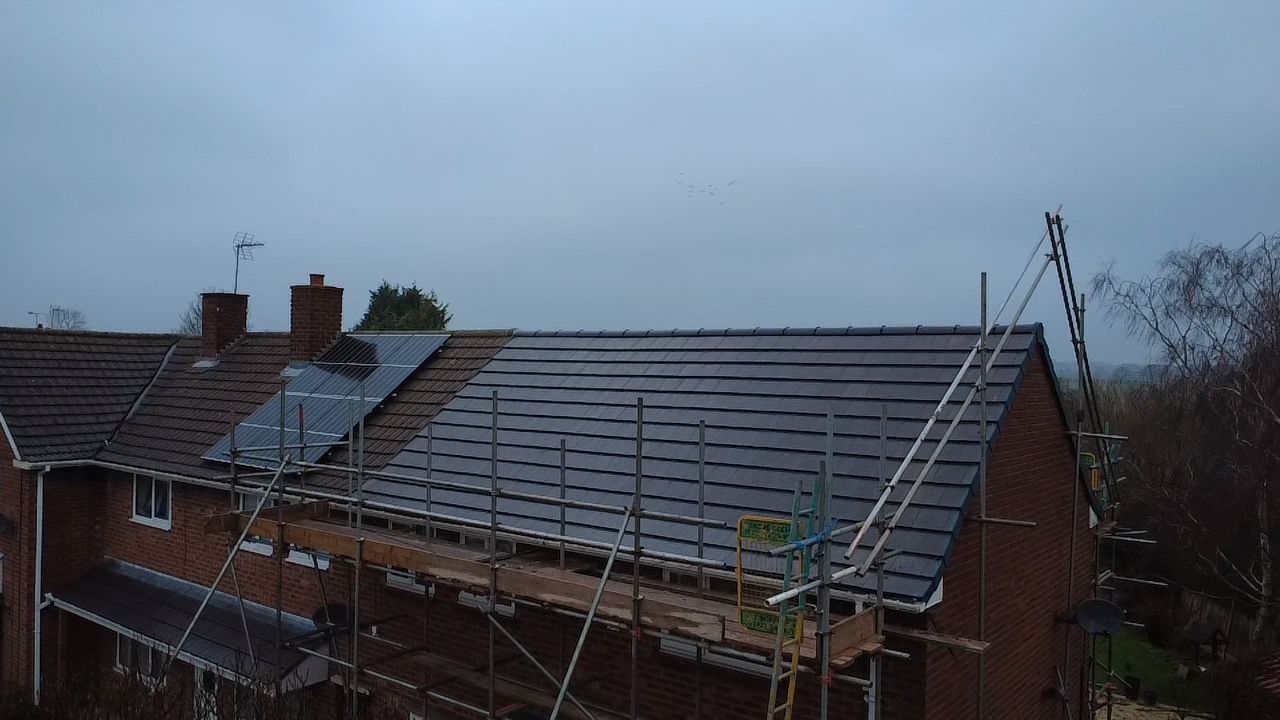 A house roof under construction, featuring new dark tiles, partially installed solar panels, and surrounding scaffolding.