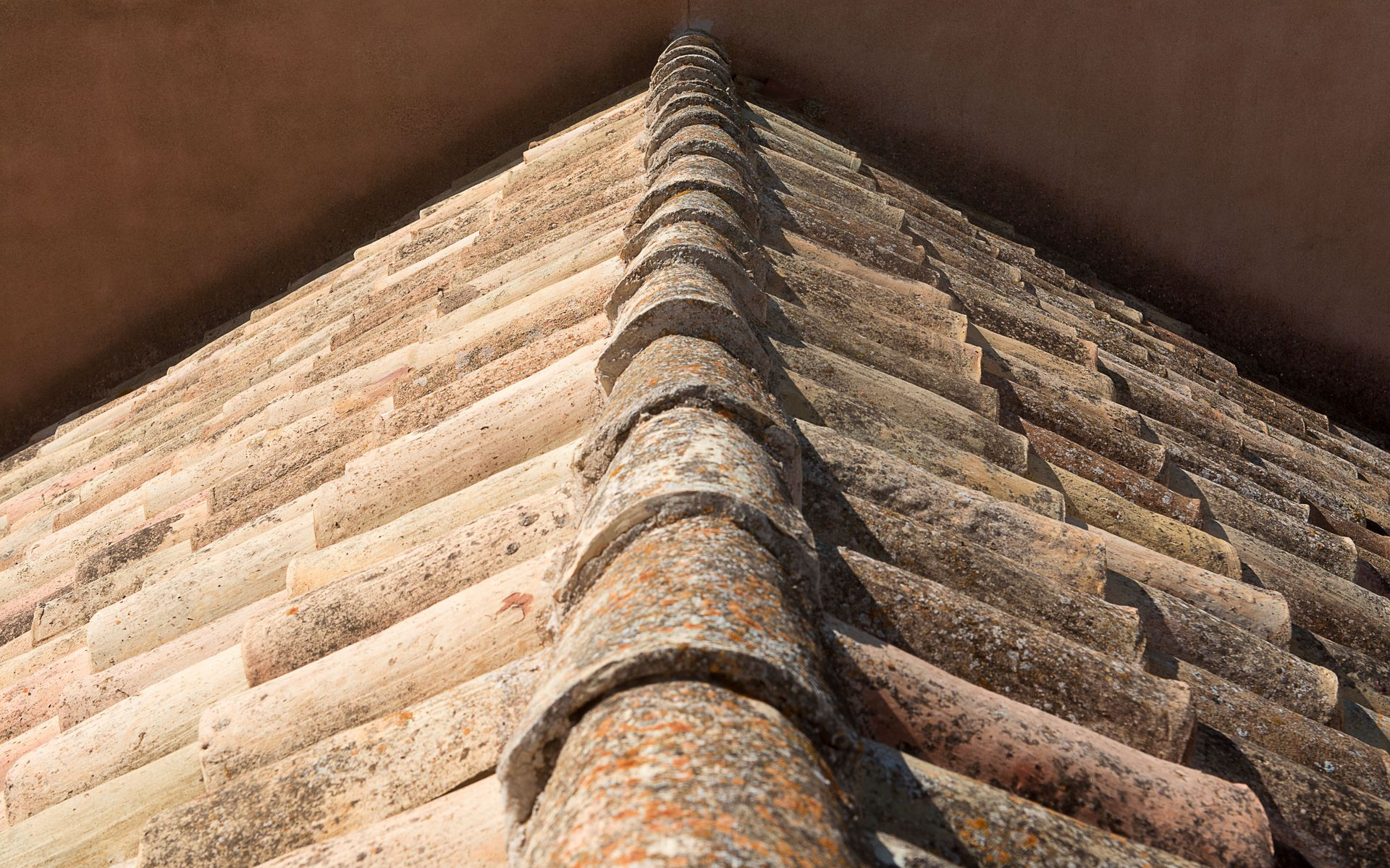Close-up of a weathered tiled roof corner meeting at a ridge against a dark background.