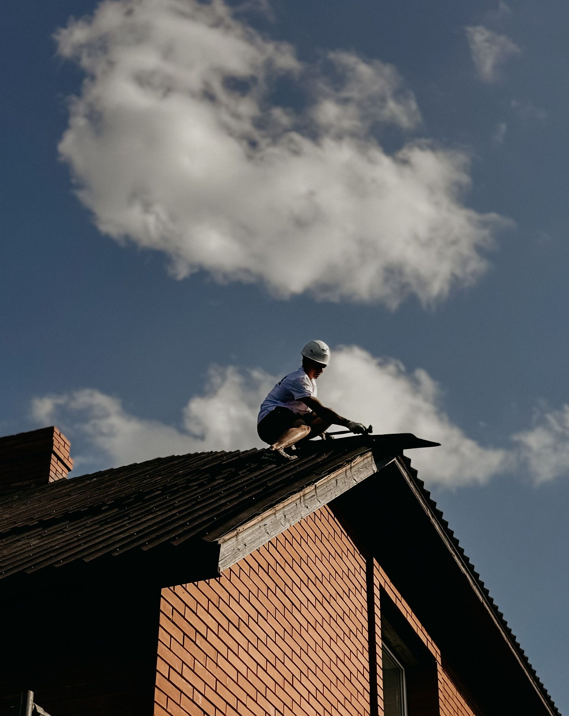 Person working on a brick roof under a cloudy sky.