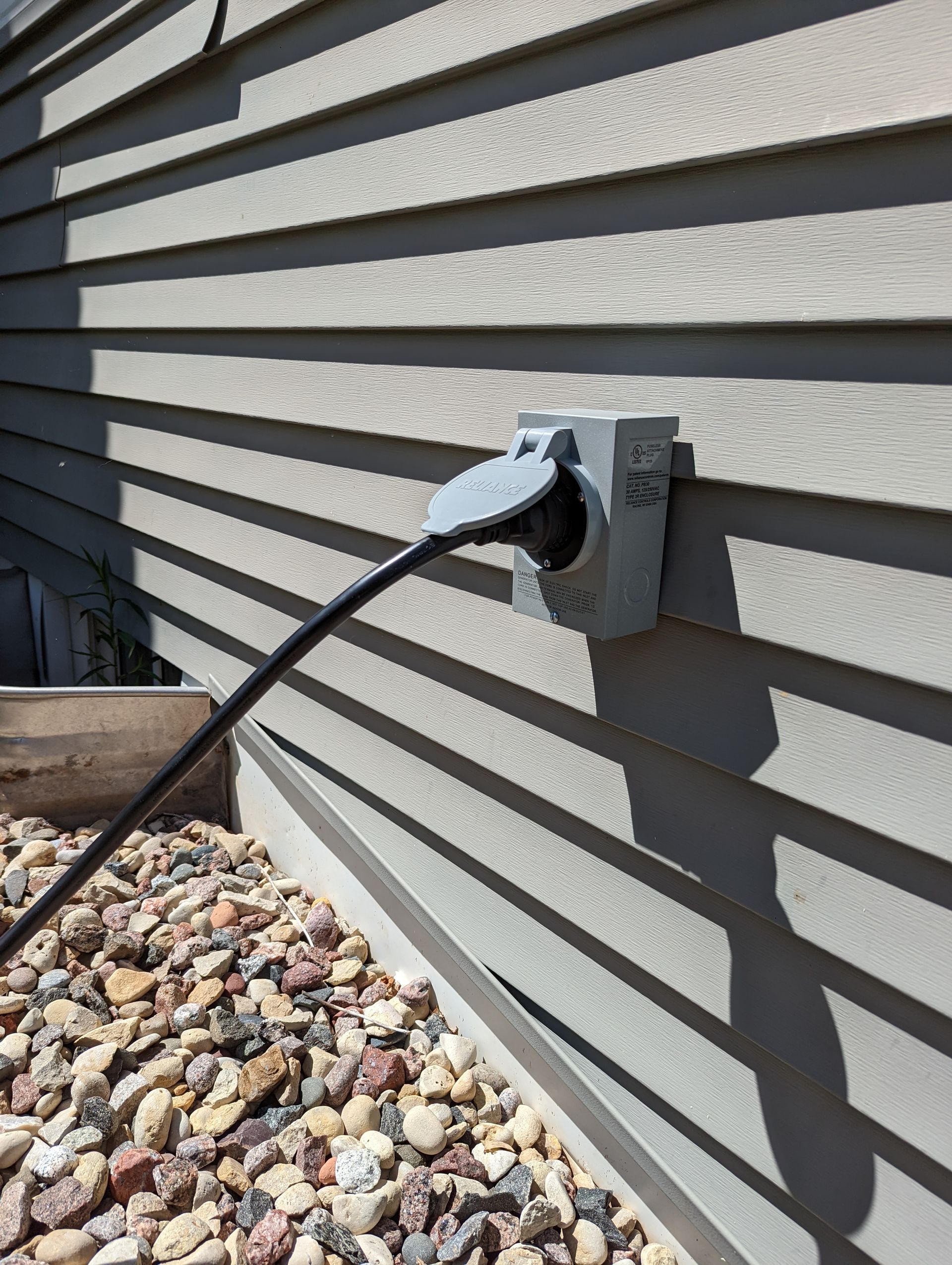 A power cord is plugged into a socket on the side of a house.