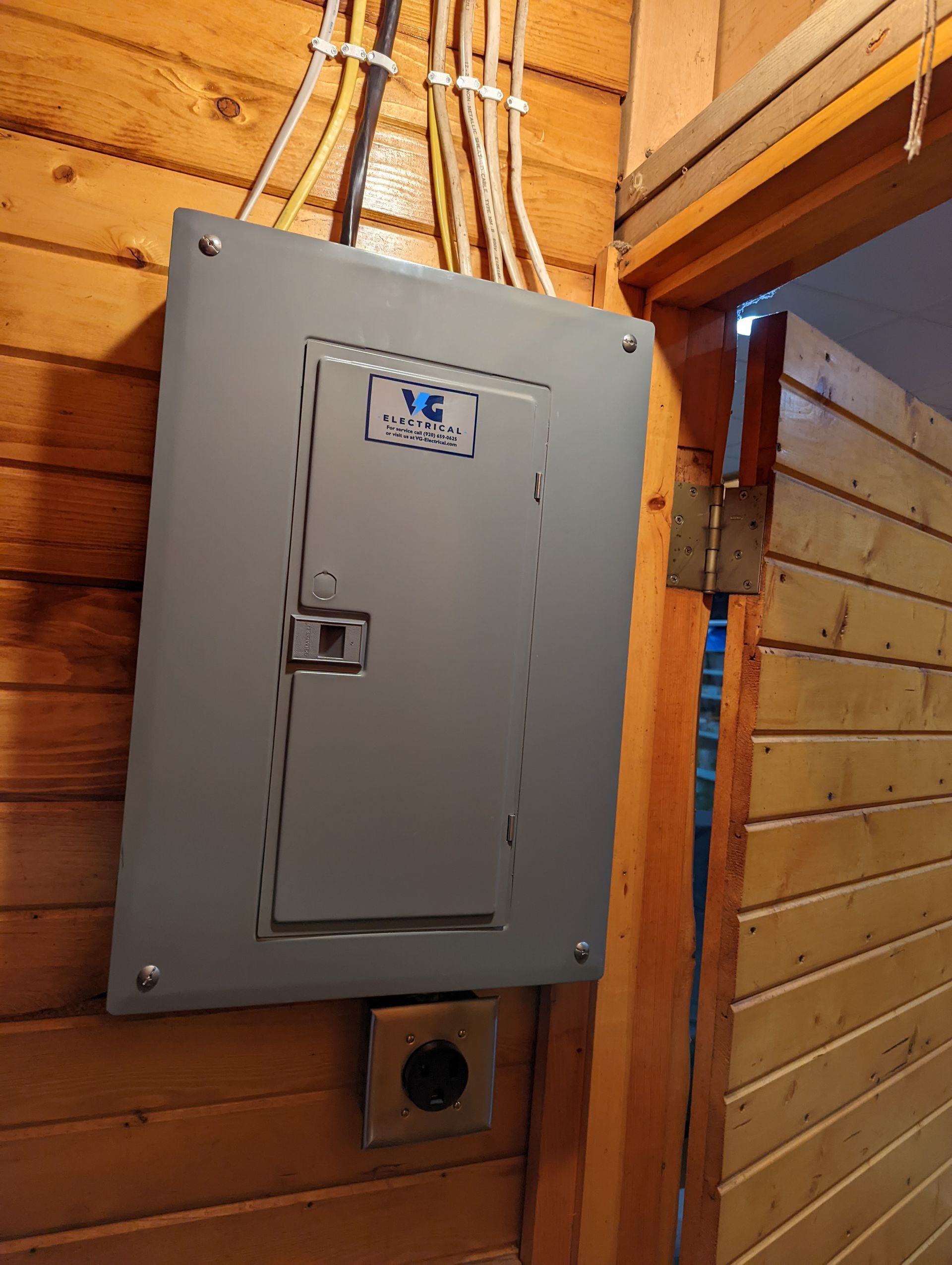 An electrical box is hanging on a wooden wall next to a door.