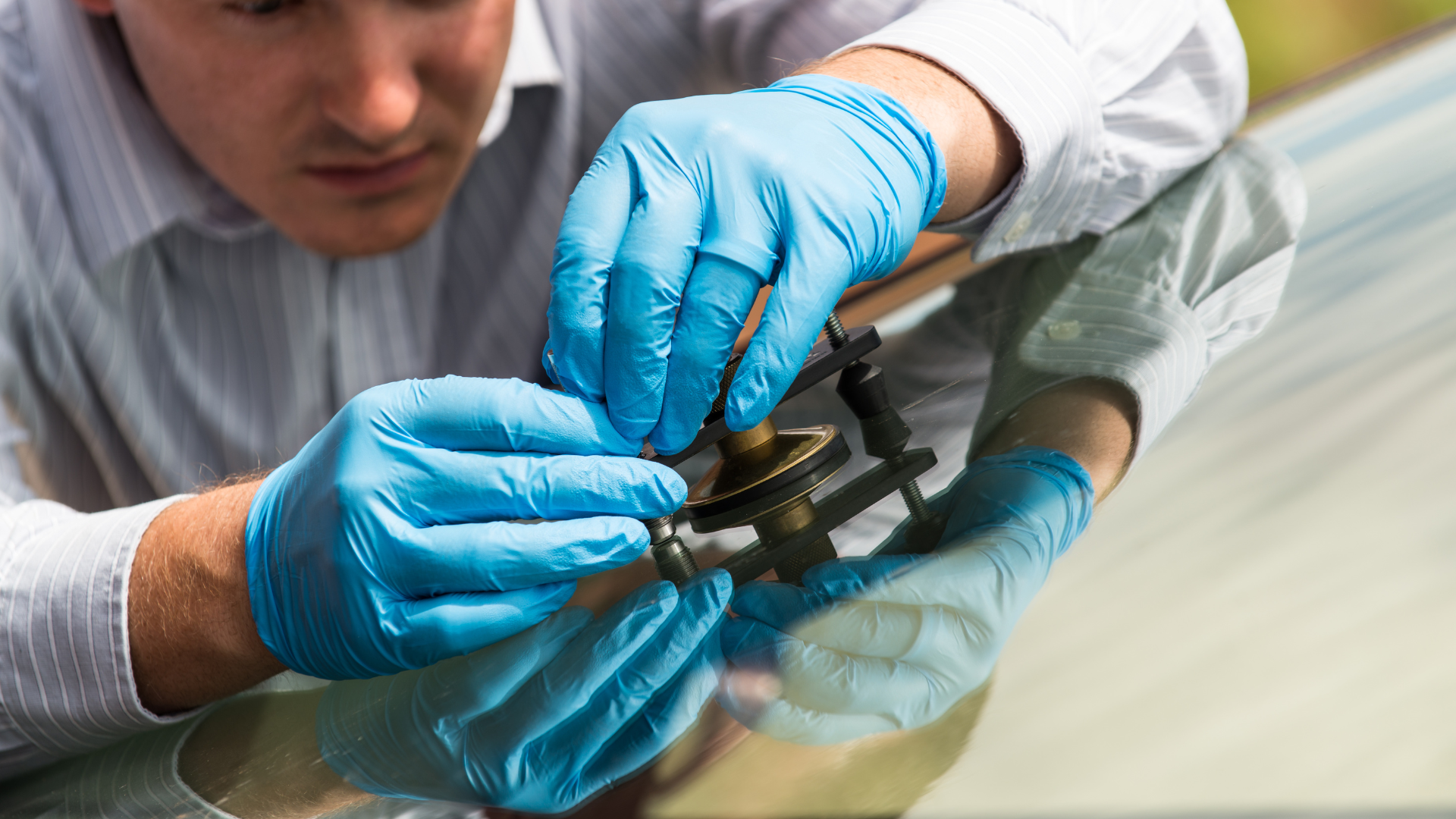 A man wearing blue gloves is repairing a cracked windshield on a car.