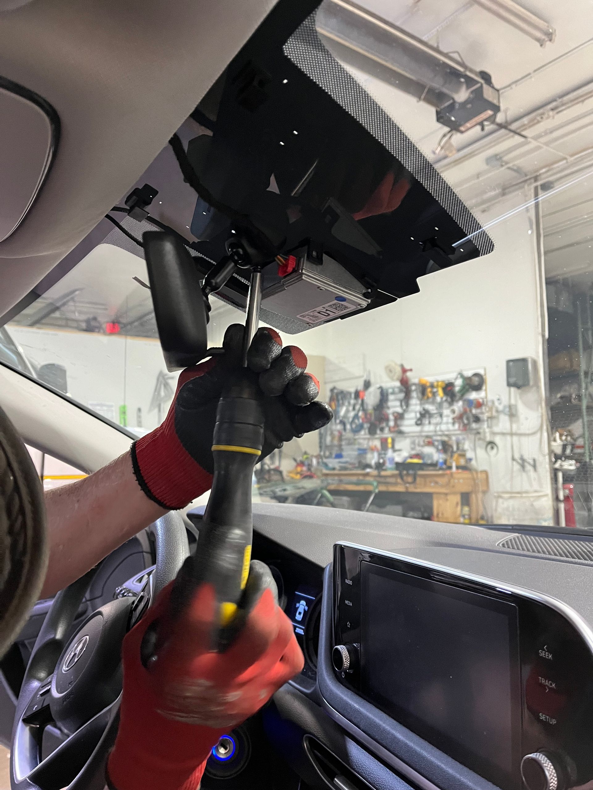 A person wearing red gloves is working on a car with a screwdriver.
