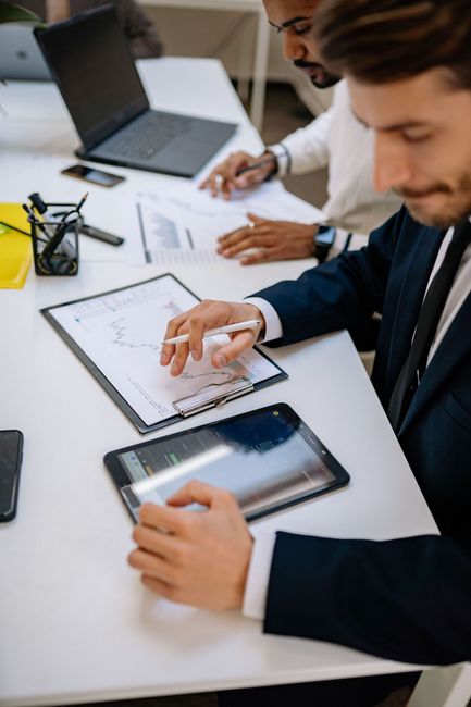 People collaborating at a desk, using a tablet, laptop, and notes in a bright office.