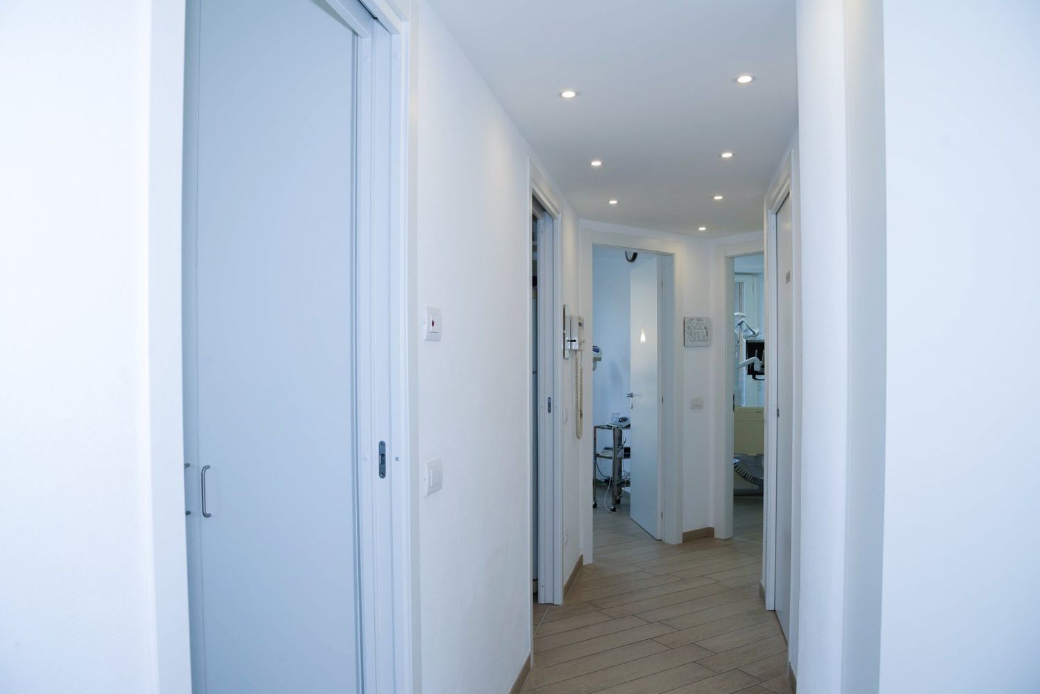 Luminoso corridoio bianco con porte aperte, faretti a incasso sul soffitto e pavimento in moquette.