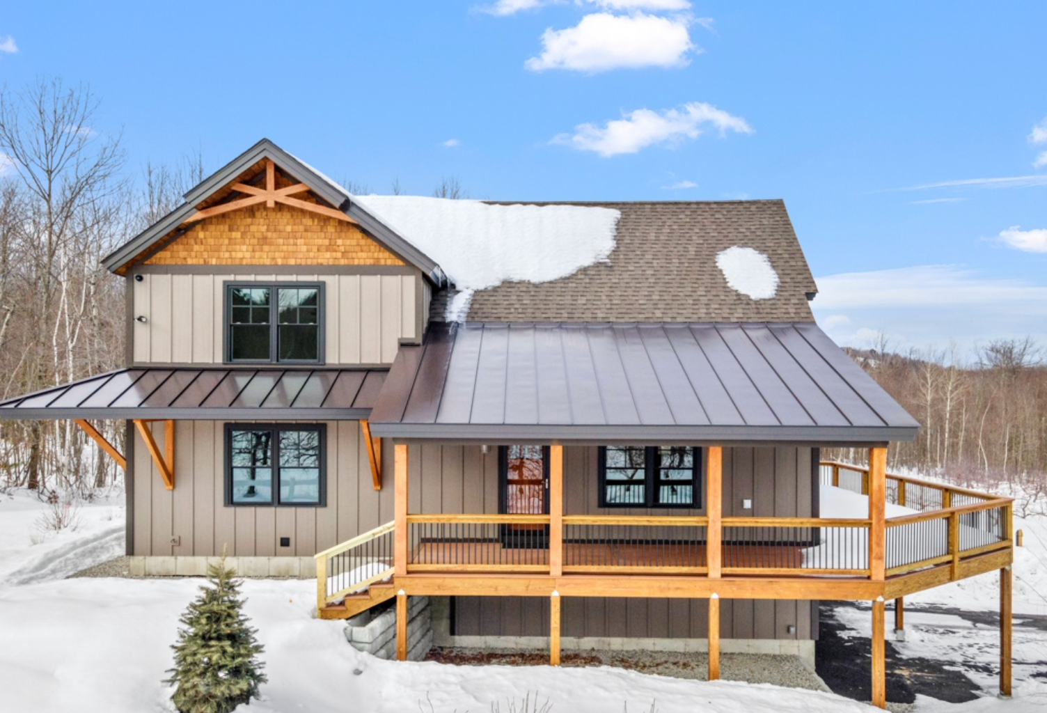 A house with a metal roof and a wooden deck in the snow.