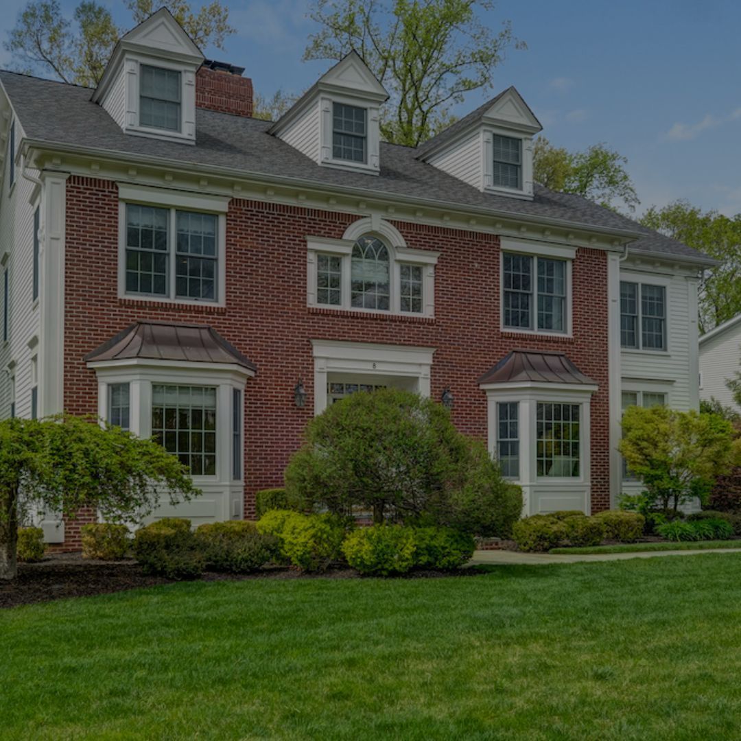 A large brick and white house with a lush green lawn in front of it