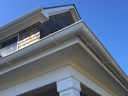 Close-up of a white house roof and corner trim against a blue sky