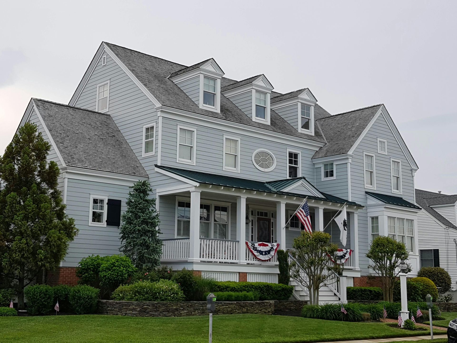 Blue house with white trim, porch, American flag, and manicured lawn.