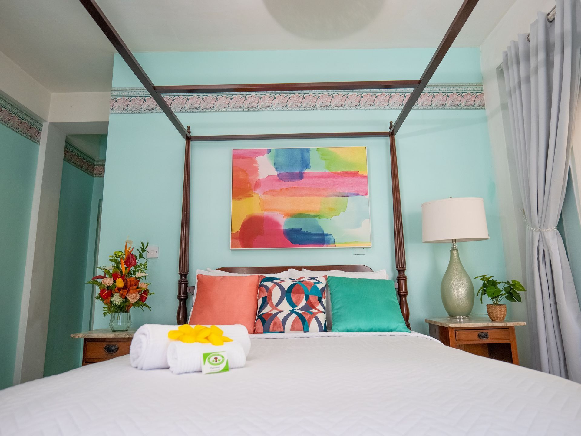 A queen bed with white linens and decorative pillows beneath a canopy frame in a room with light blue walls and art.