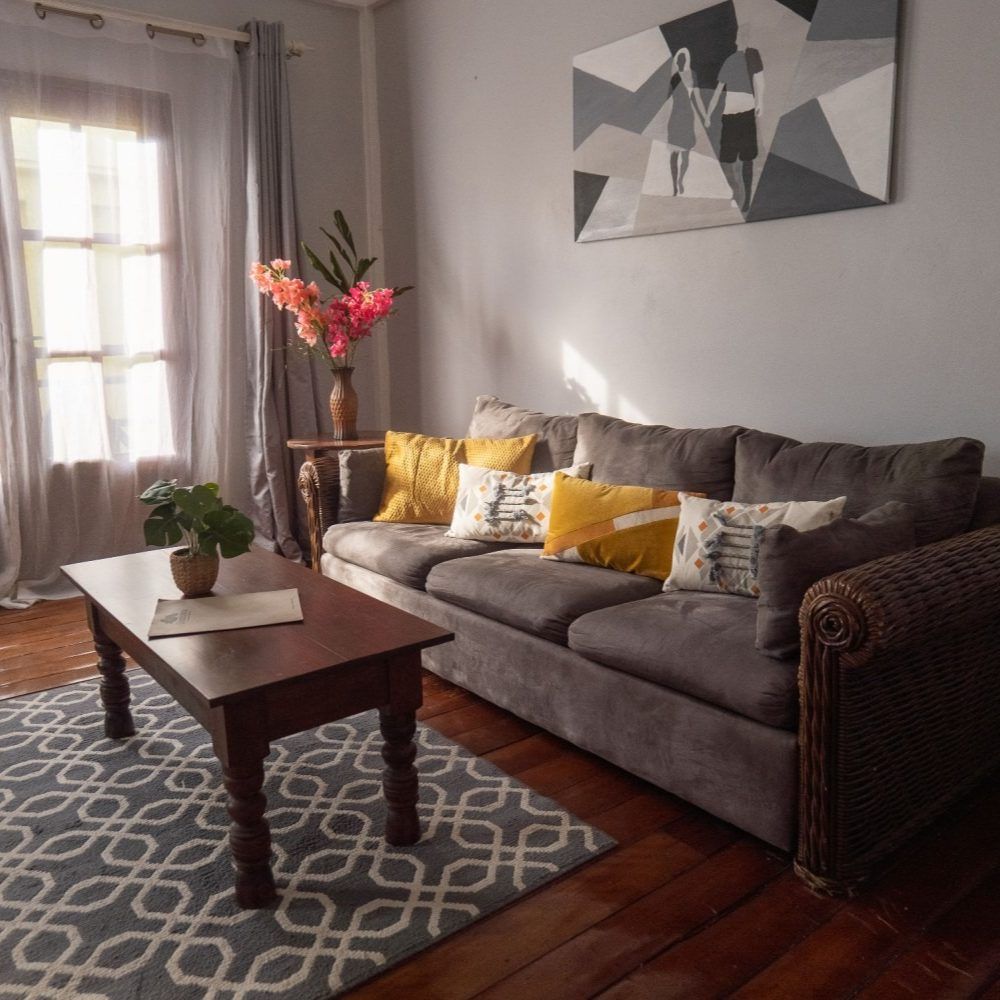 A living room featuring a grey couch with yellow and patterned pillows, a wood coffee table, and a geometric rug.