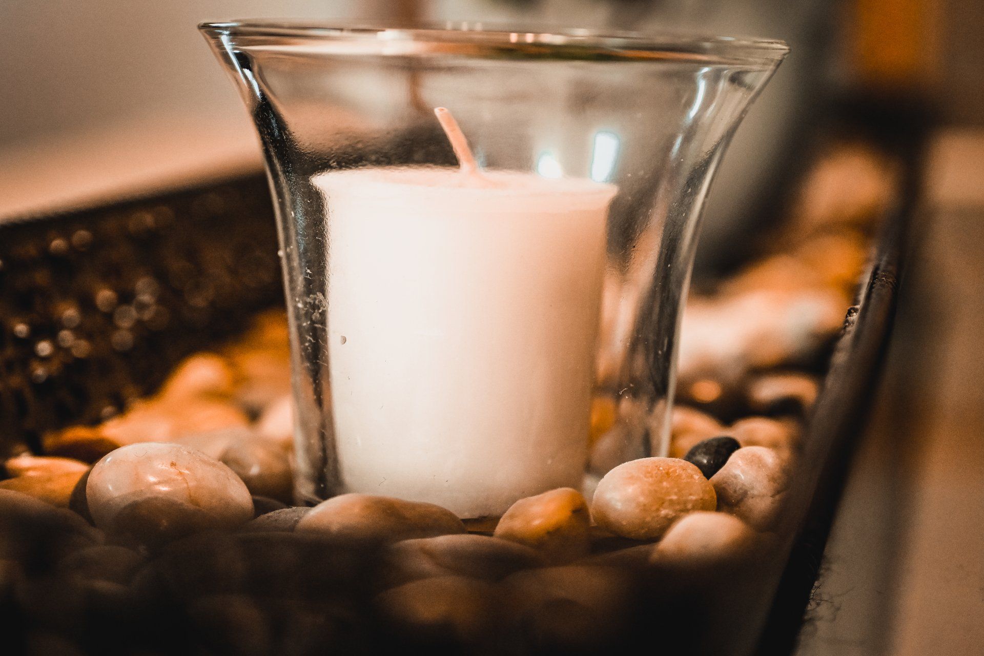 A close up of a candle in a glass surrounded by rocks.