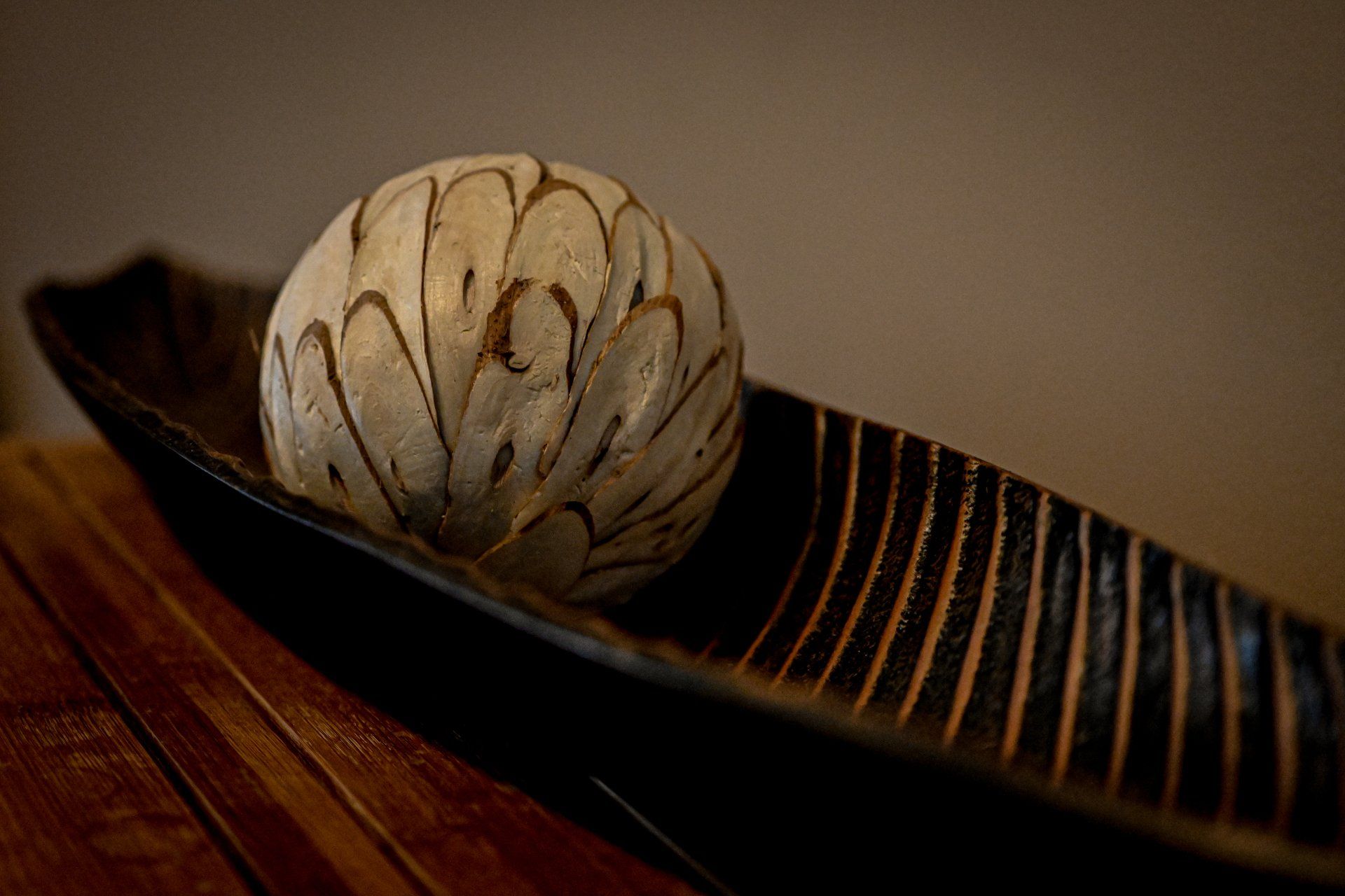 A ceramic ball is sitting on top of a striped bowl on a wooden table.