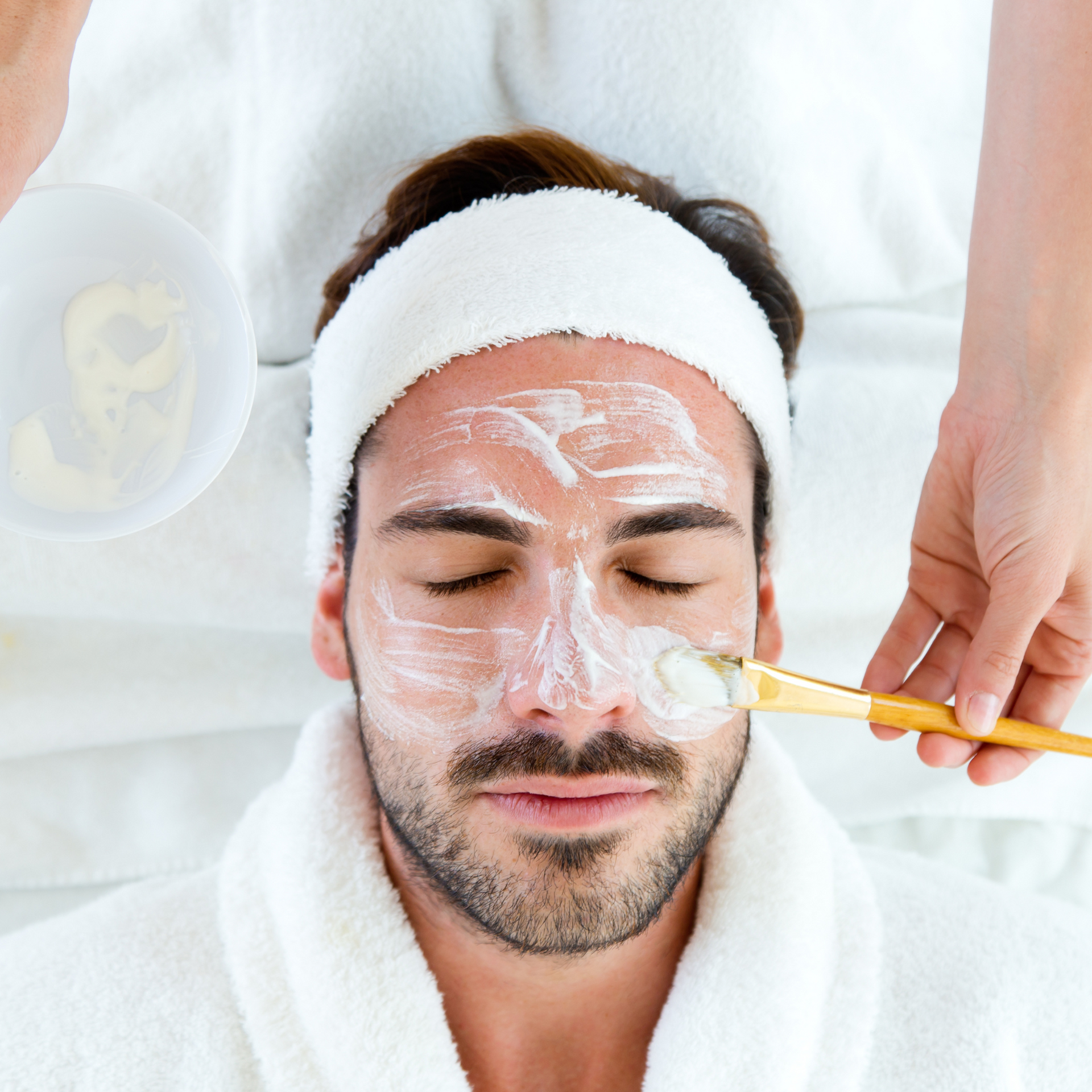 A man is getting a facial treatment with a brush