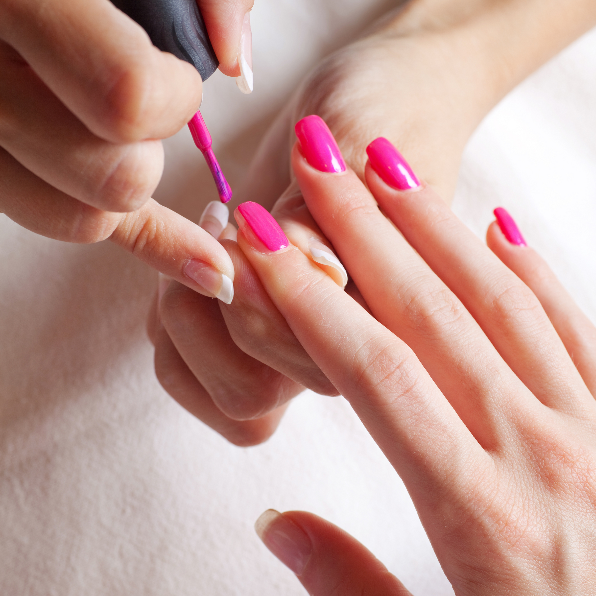 A woman is getting her nails painted with pink nail polish
