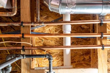 Exposed copper and PVC plumbing pipes in unfinished wooden wall framing