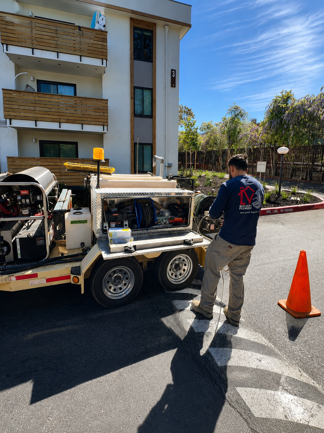 Worker beside utility truck and orange cone outside an apartment building on a sunny day