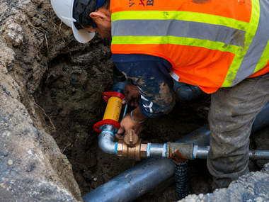 Worker in orange safety vest repairing underground pipe in a trench