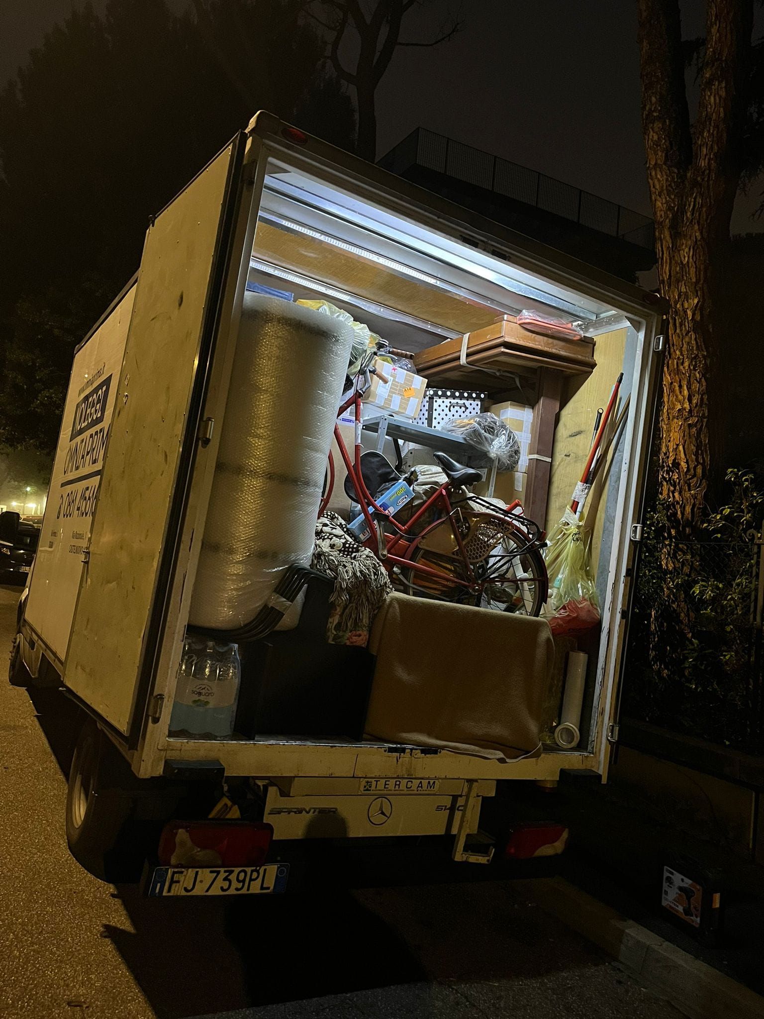 Un camion per traslochi con il retro aperto, pieno di oggetti per la casa. Illuminato di notte.