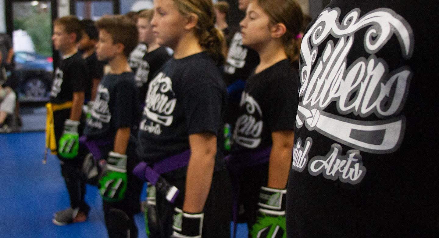 a group of young children are standing in a line wearing boxing gloves .