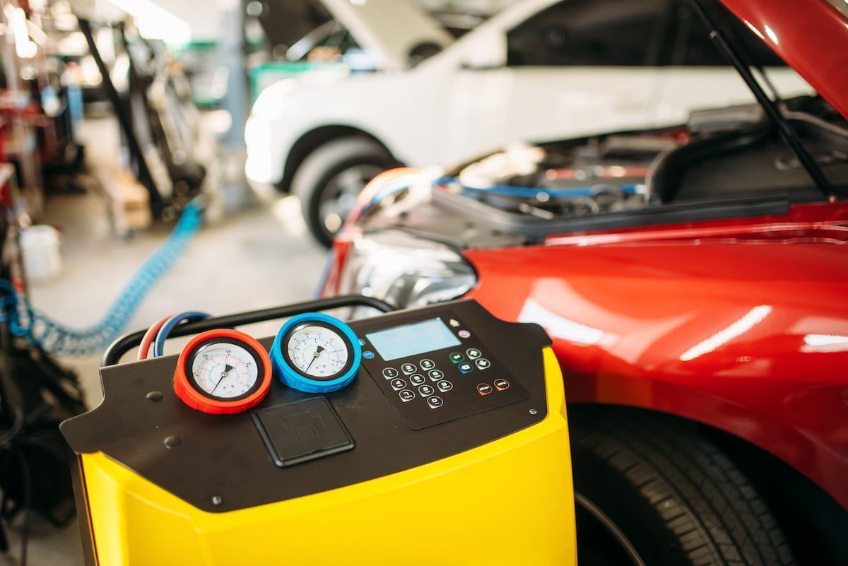 A red car with an open hood being serviced by a yellow air conditioning machine. | Ben's Automotive