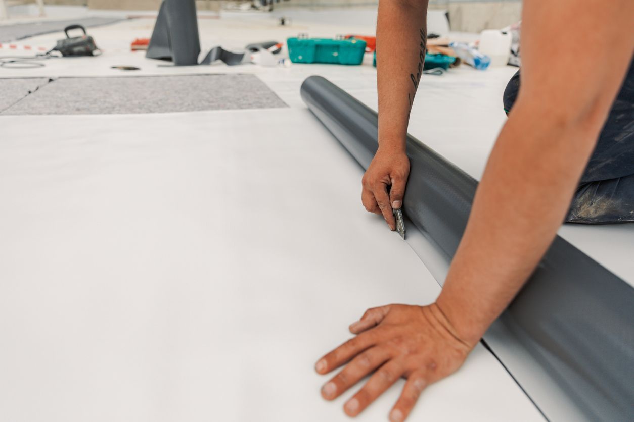 A man is cutting a roll of vinyl flooring on the floor.