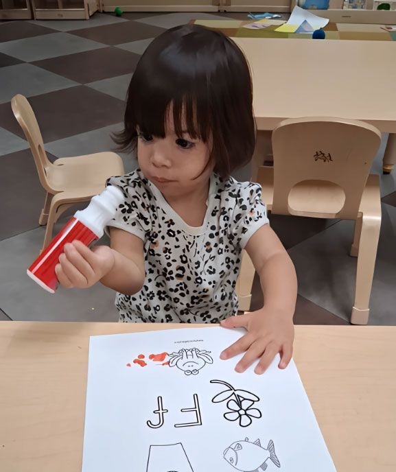 Montessori child coloring with a red marker at a table.
