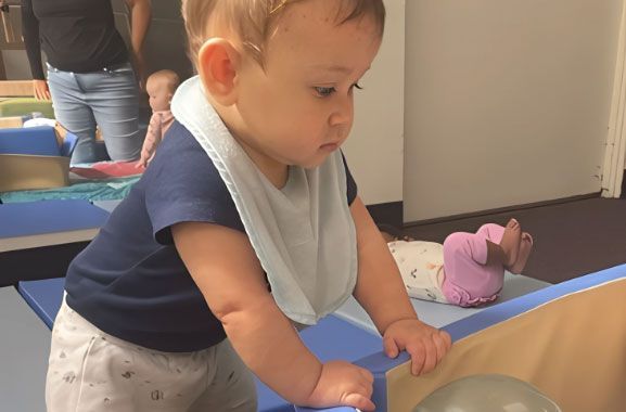 Montessori infant pulling up on soft blocks in the Nido classroom.